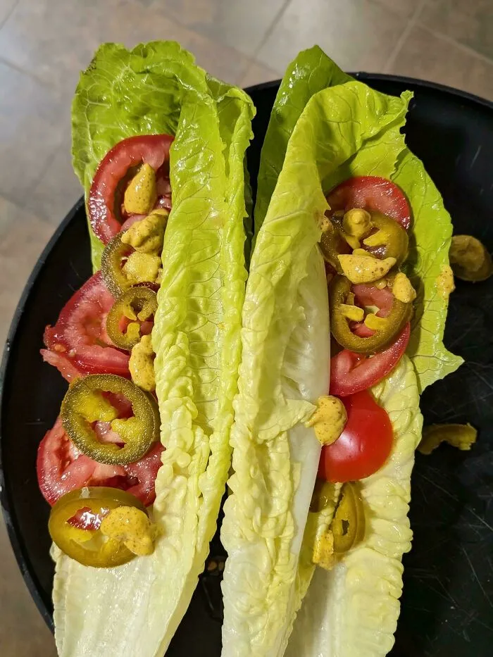 Lettuce wraps with tomatoes, jalapeños, and mustard, appearing as unappetizing, disgusting food.