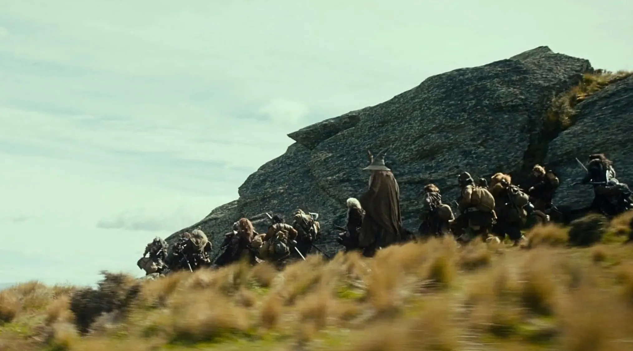 The Hobbit dwarves and Gandalf journey across a grassy hill towards a mountain in their quest for the underground kingdom.