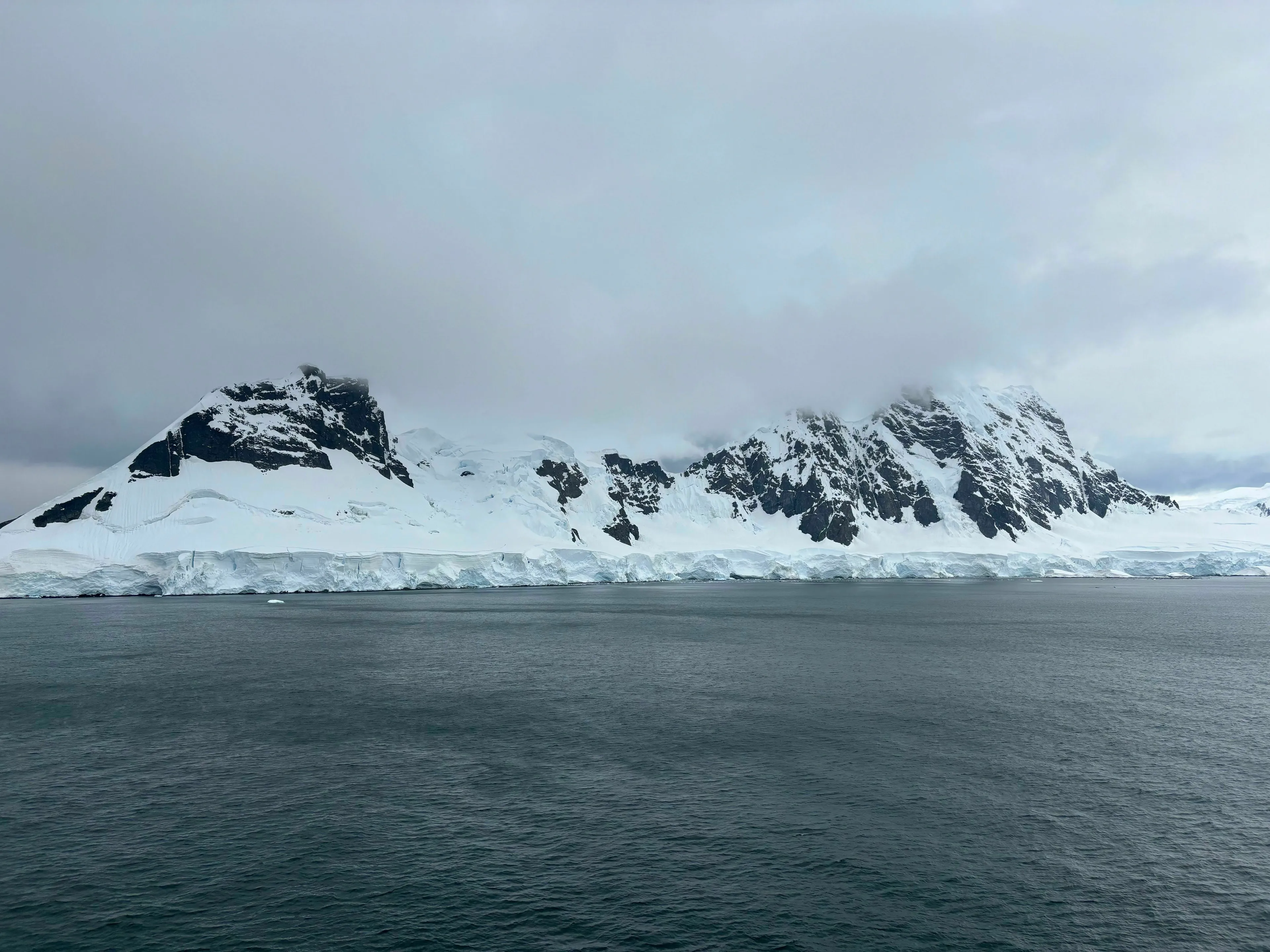 A vast, icy landscape of the South Pole with snow-covered mountains and open water.