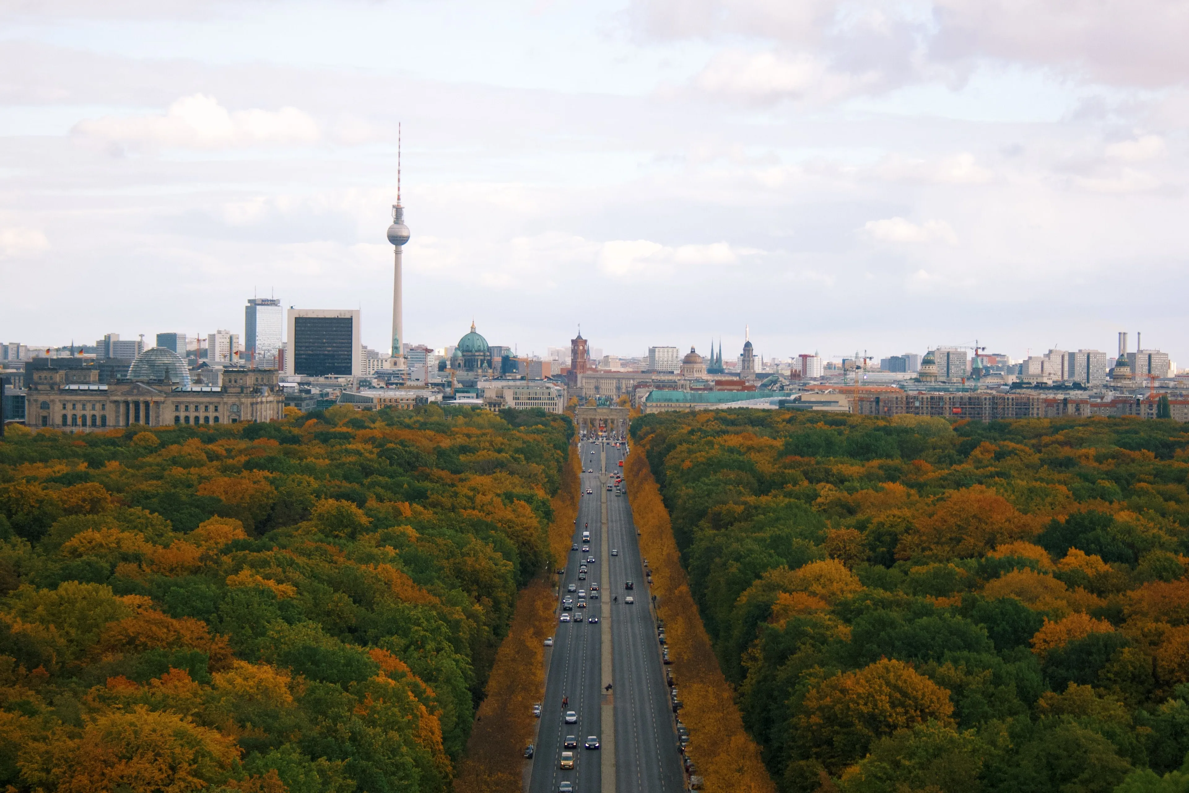 An aerial view of Berlin, Germany's most populated city, showing a wide road lined with trees and city buildings.