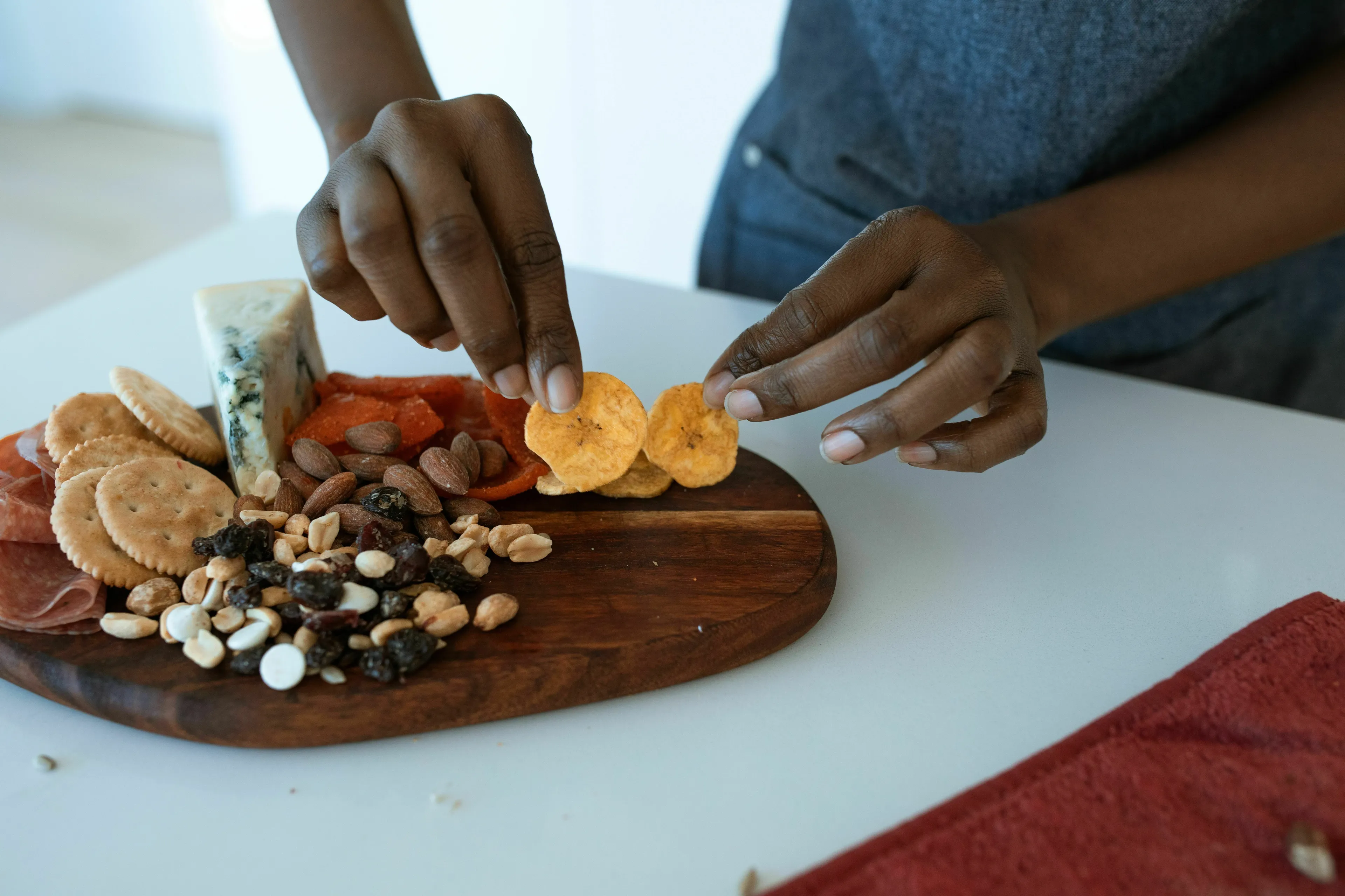 Hands arranging a snack platter with plantain chips, nuts, crackers, cheese, and cured meats. A delicious mystery snack.