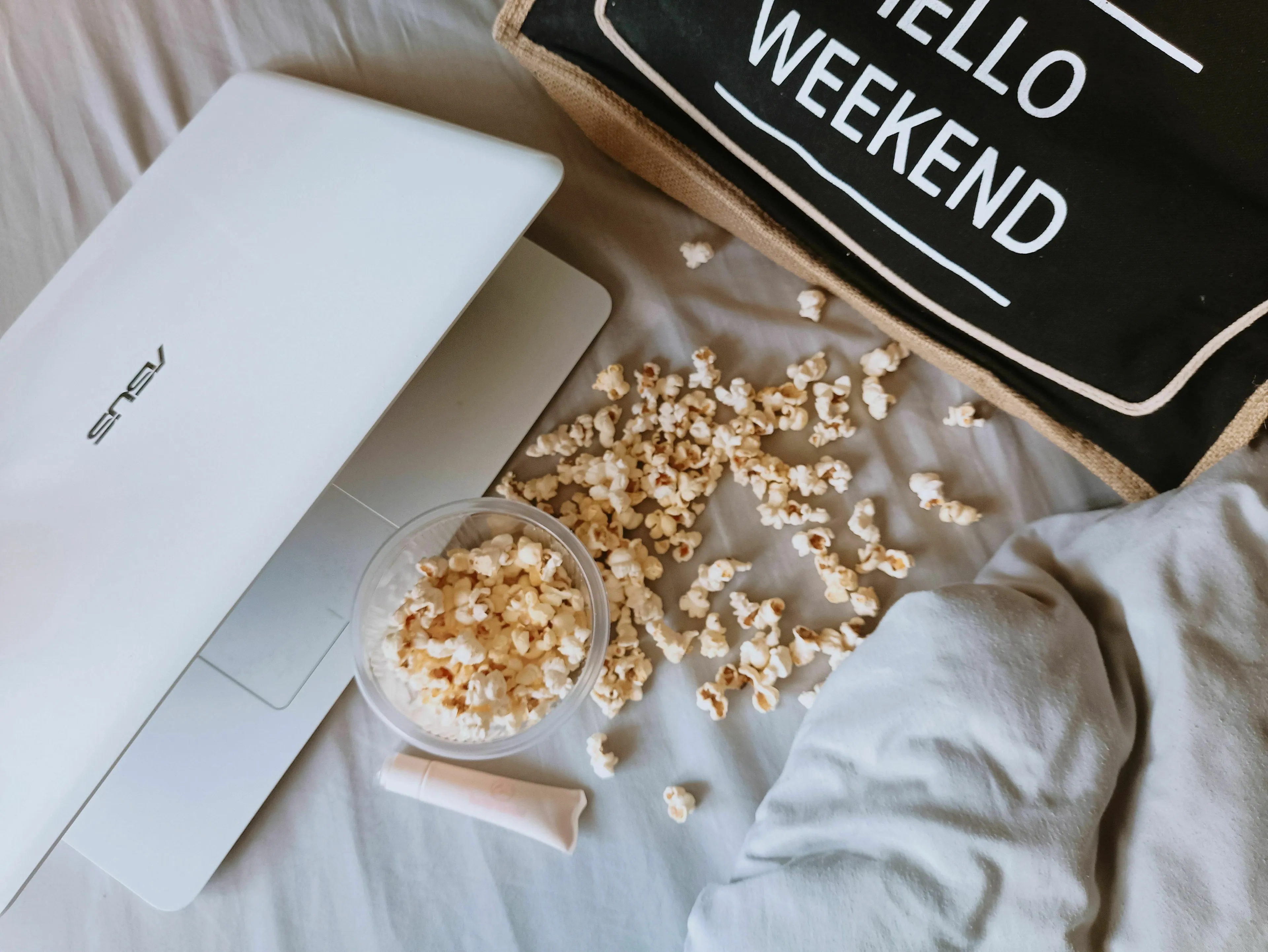 A cozy weekend scene with a laptop, popcorn, and a bag saying Hello Weekend, perfect for an unresolved mystery.