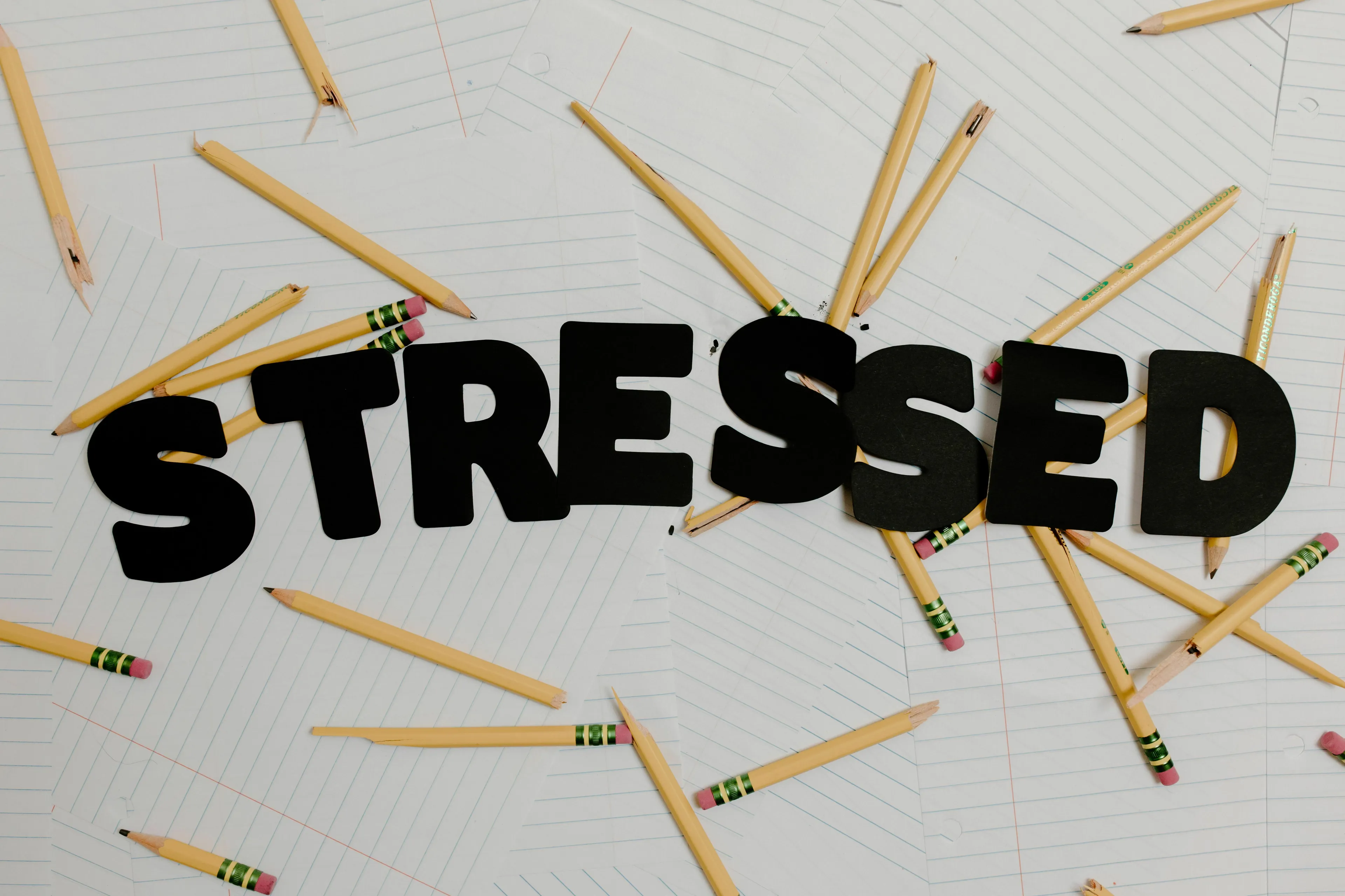The word STRESSED in black letters surrounded by broken pencils on a white background.