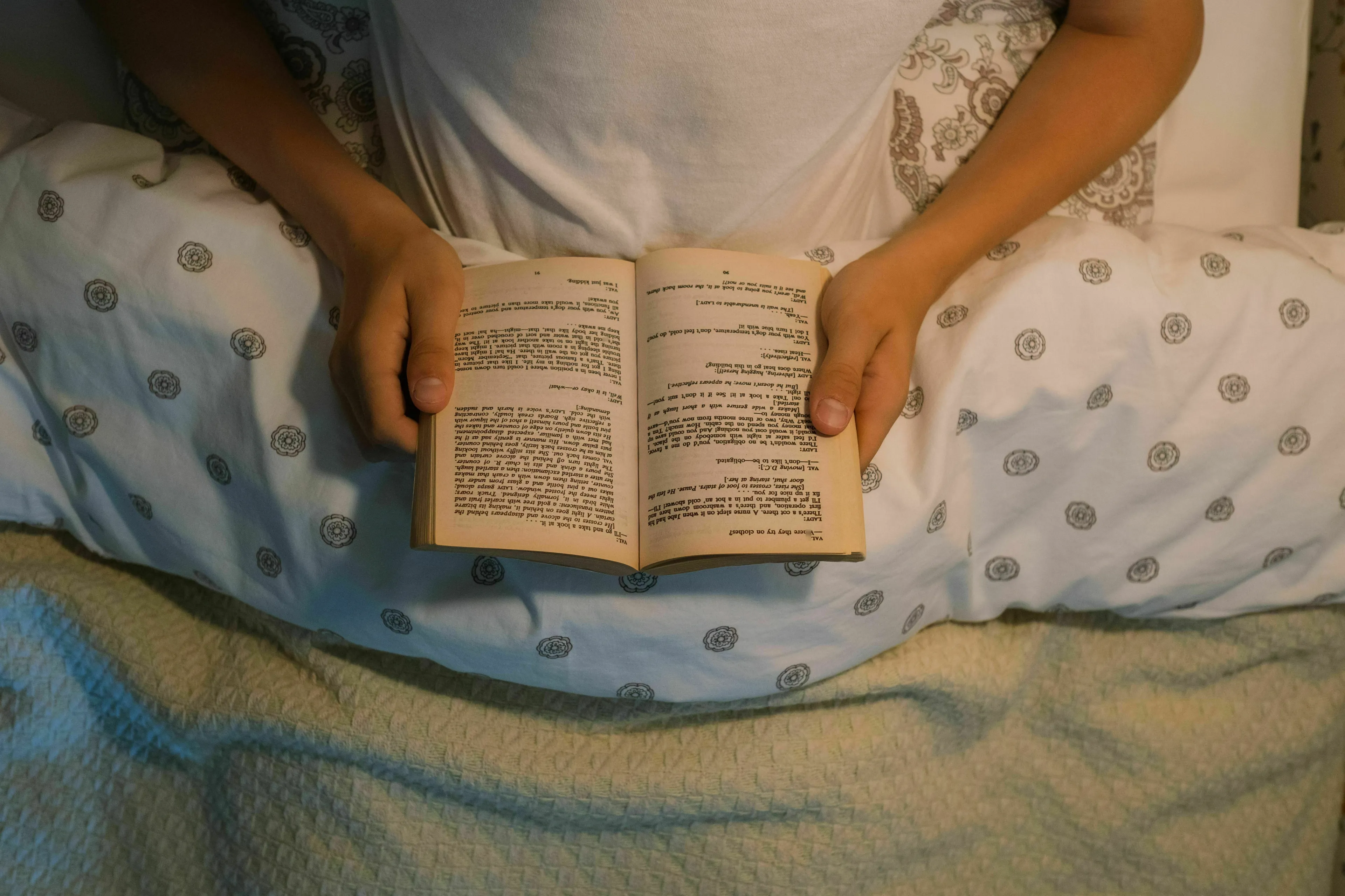 A person in bed, holding an open book, representing the main SEO keyword: bedtime read.