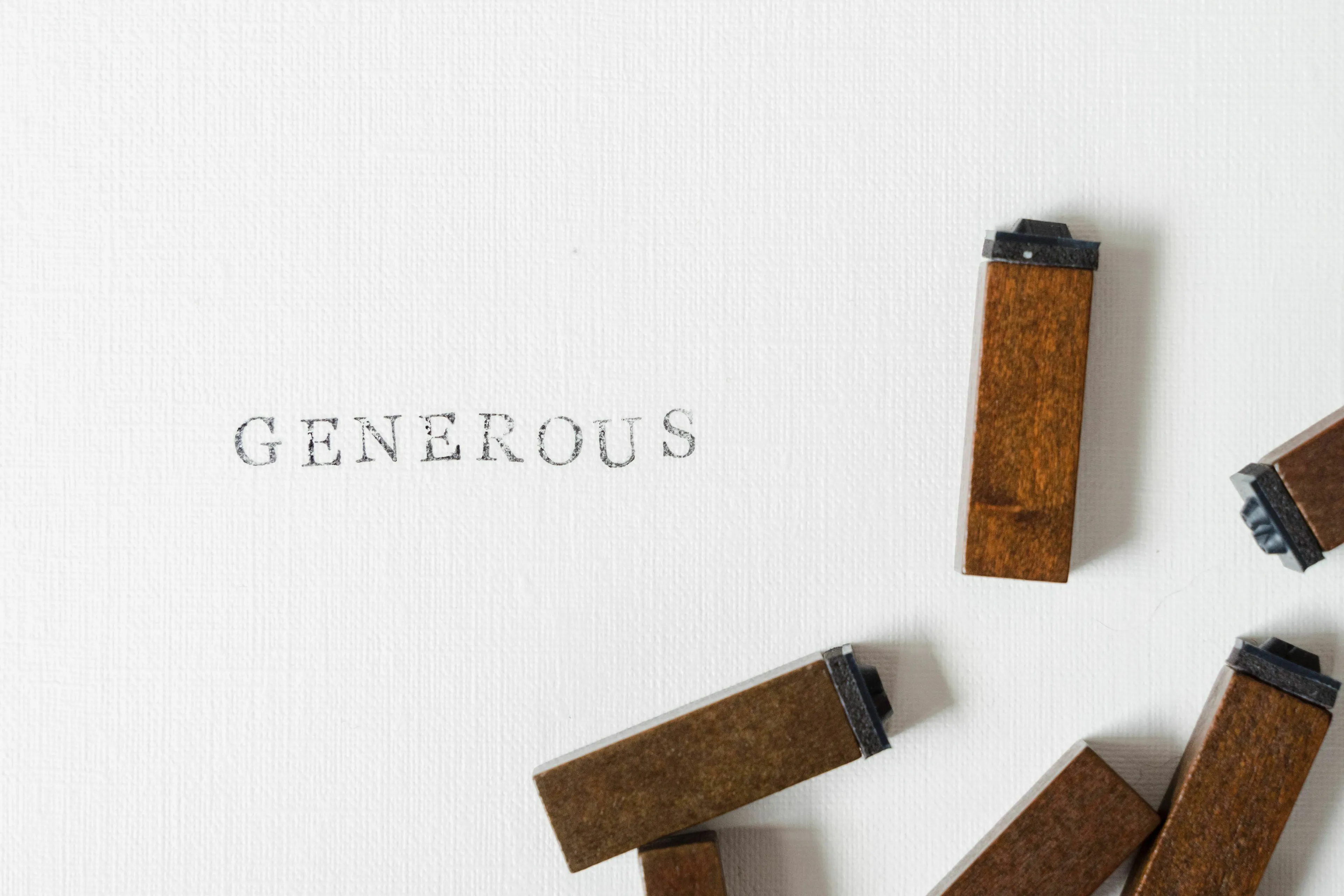 The word generous typed on white paper with wooden letter blocks scattered around, representing a generous meal.