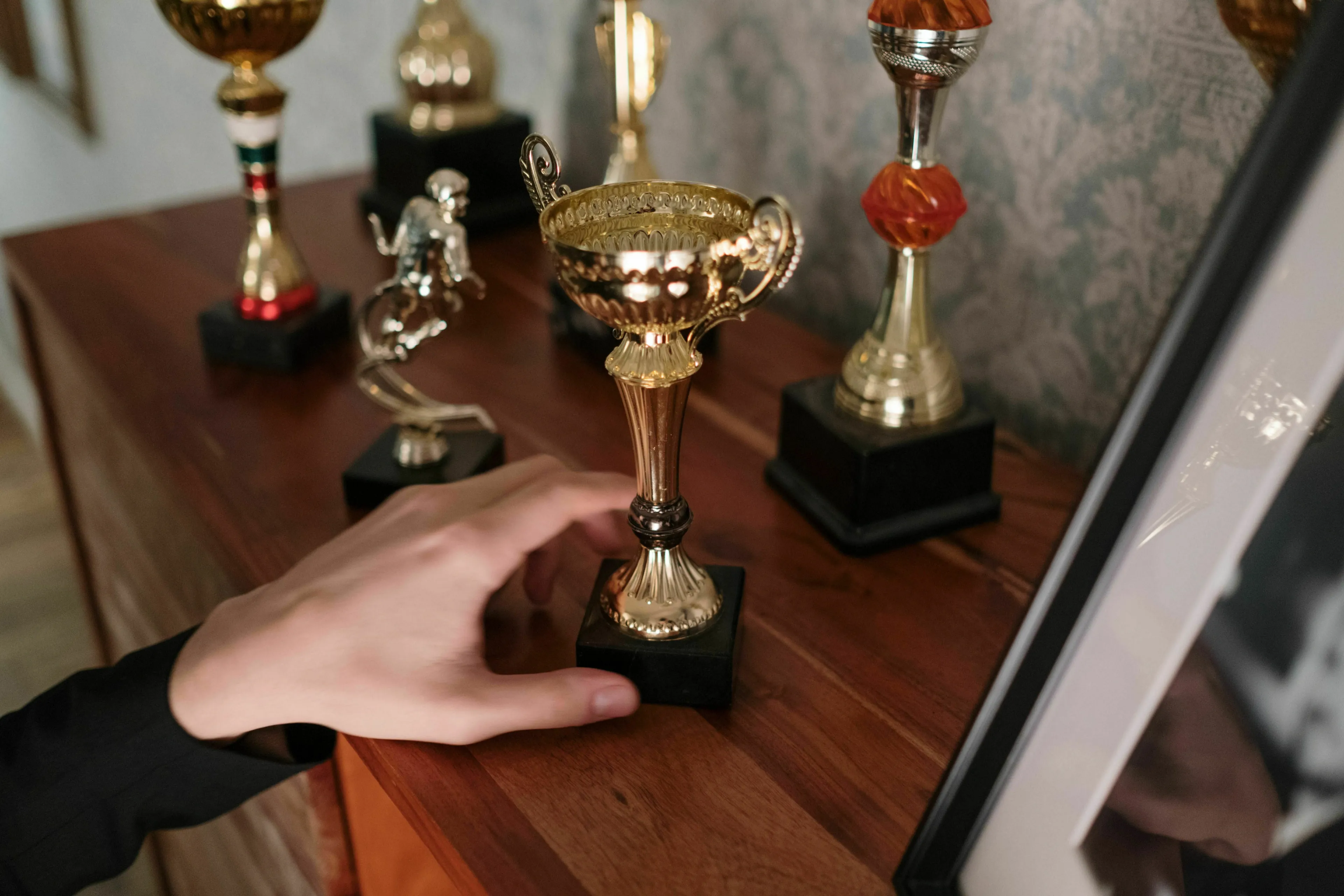 A hand reaching for a golden trophy among others, signifying a movie villain's reaction to rivalry.