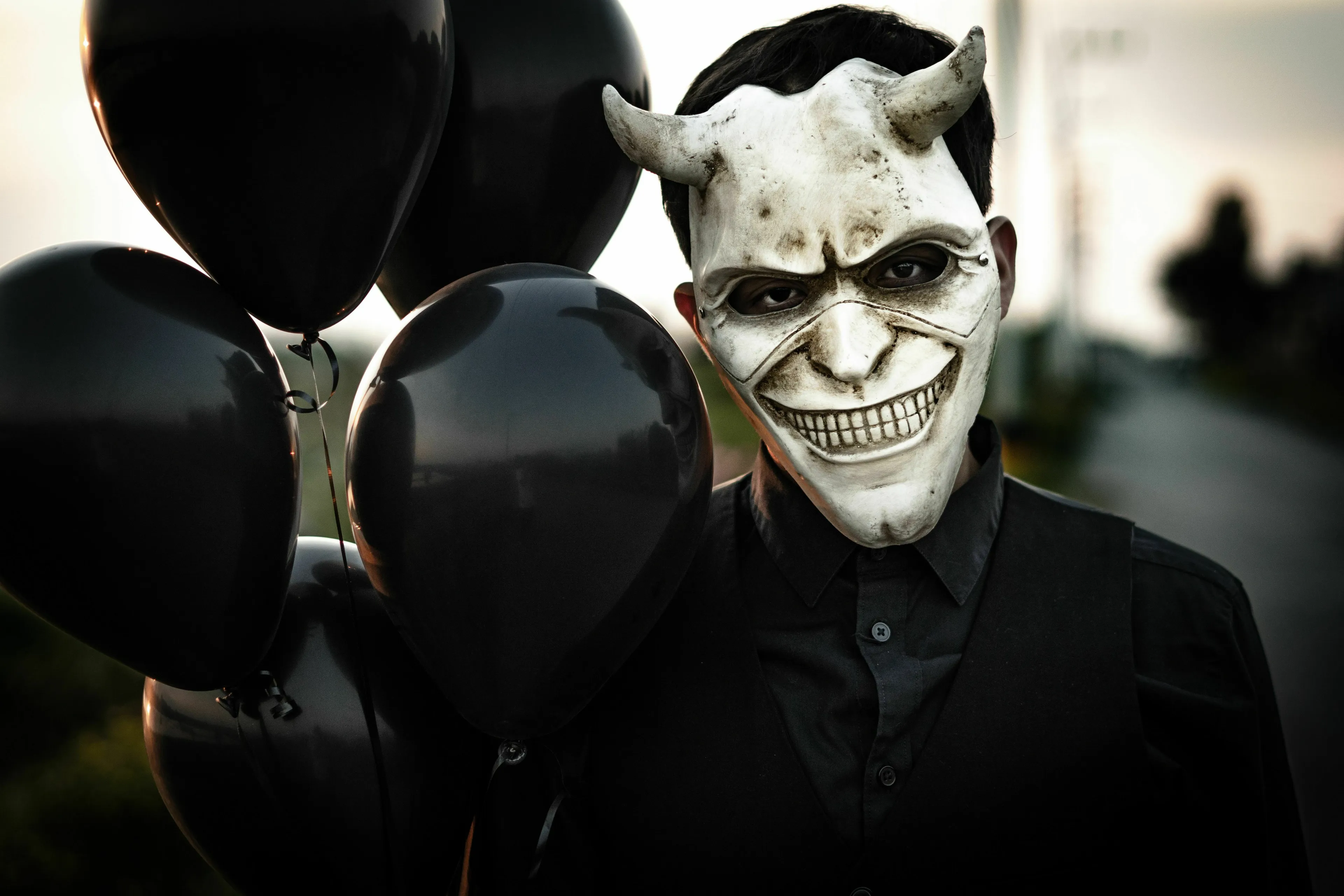 Person in a horned mask holding black balloons, reflecting a movie villain's lair aesthetic.