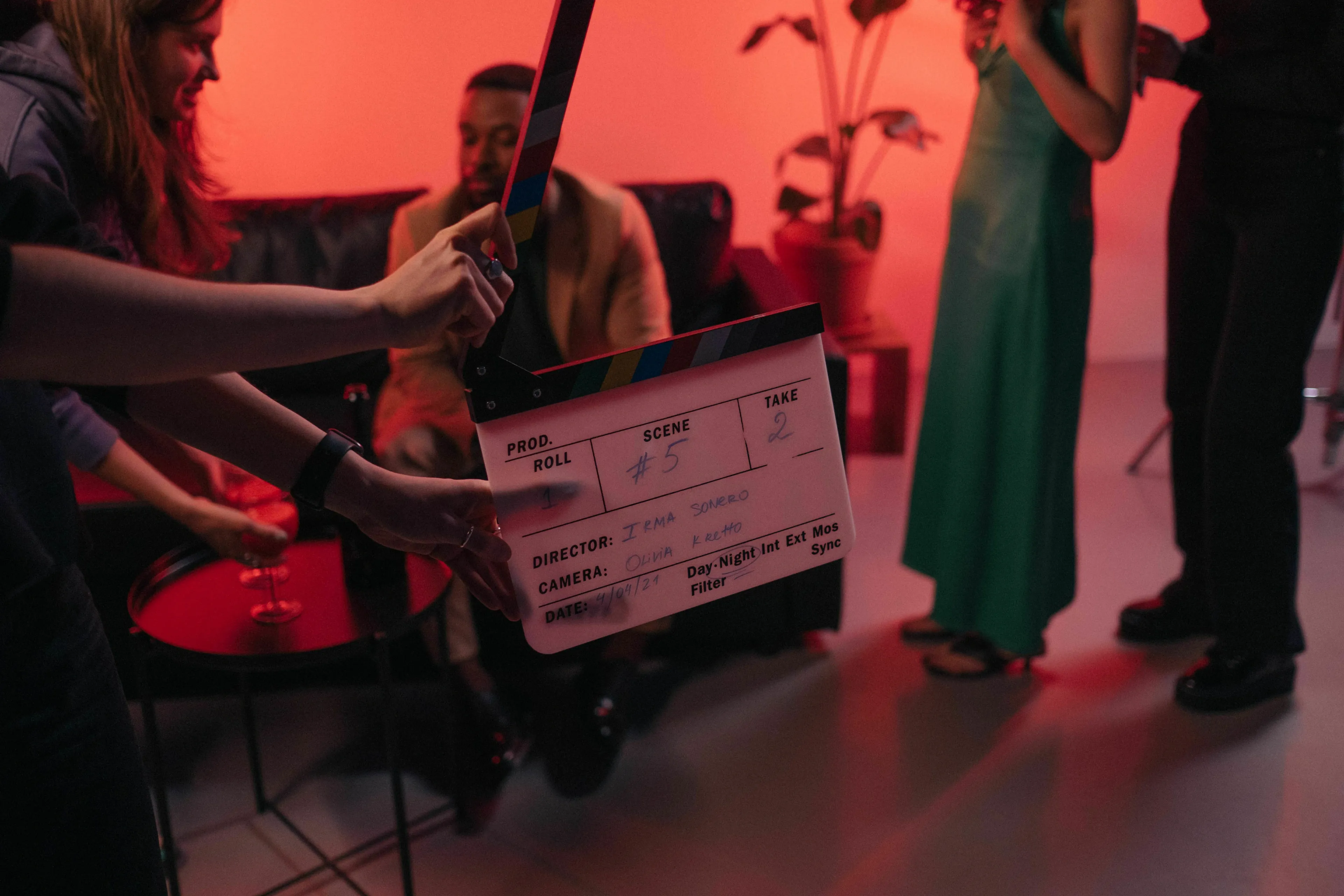 Film set with a clapperboard in the foreground, recording a scene with a movie villain in a red-lit room.