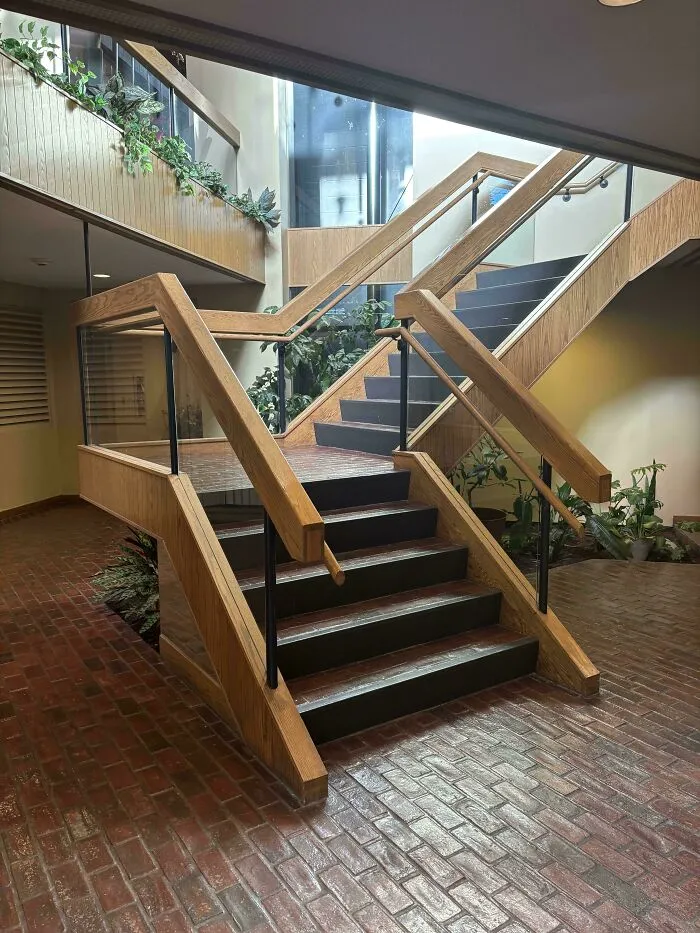 An indoor atrium with wooden staircases and lush plants, characteristic of 90s architectural styles.