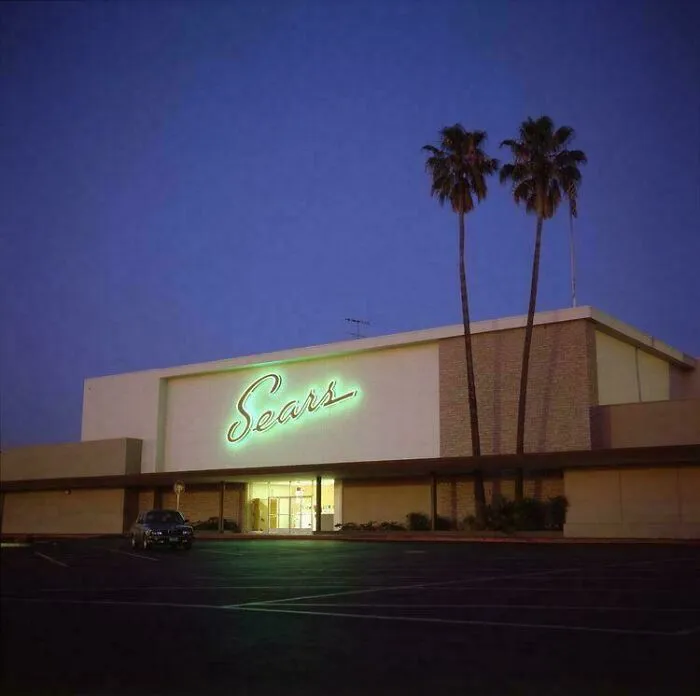 A glowing Sears sign at dusk with palm trees, evoking nostalgia for life in the 90s.