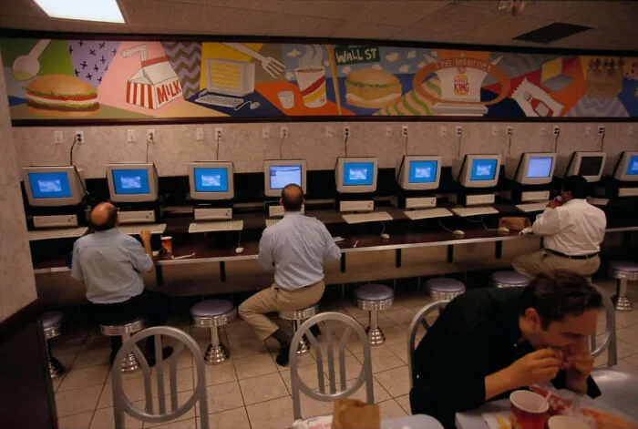 A row of people using computers at an internet cafe, a common scene from life in the 90s.