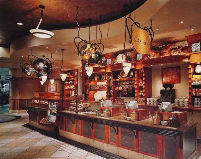 An old-school restaurant interior with hanging signs for desserts, salads, and cashier, reminiscent of life in the 90s.