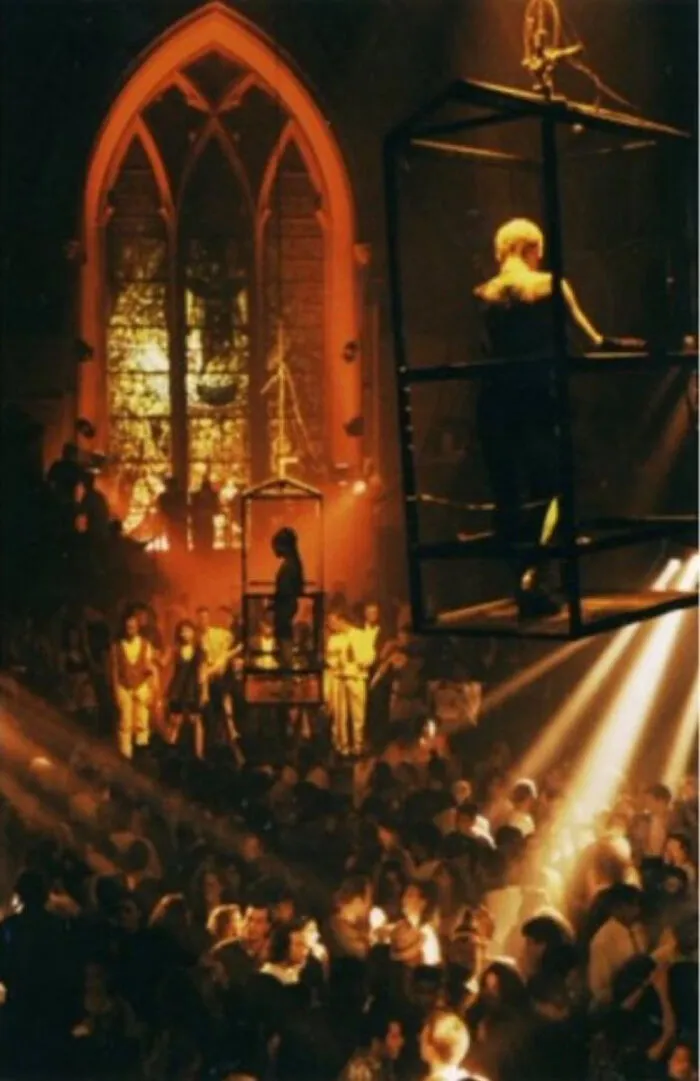 A crowded 90s nightclub in a church with dancers in cages, reflecting 90s life and time.