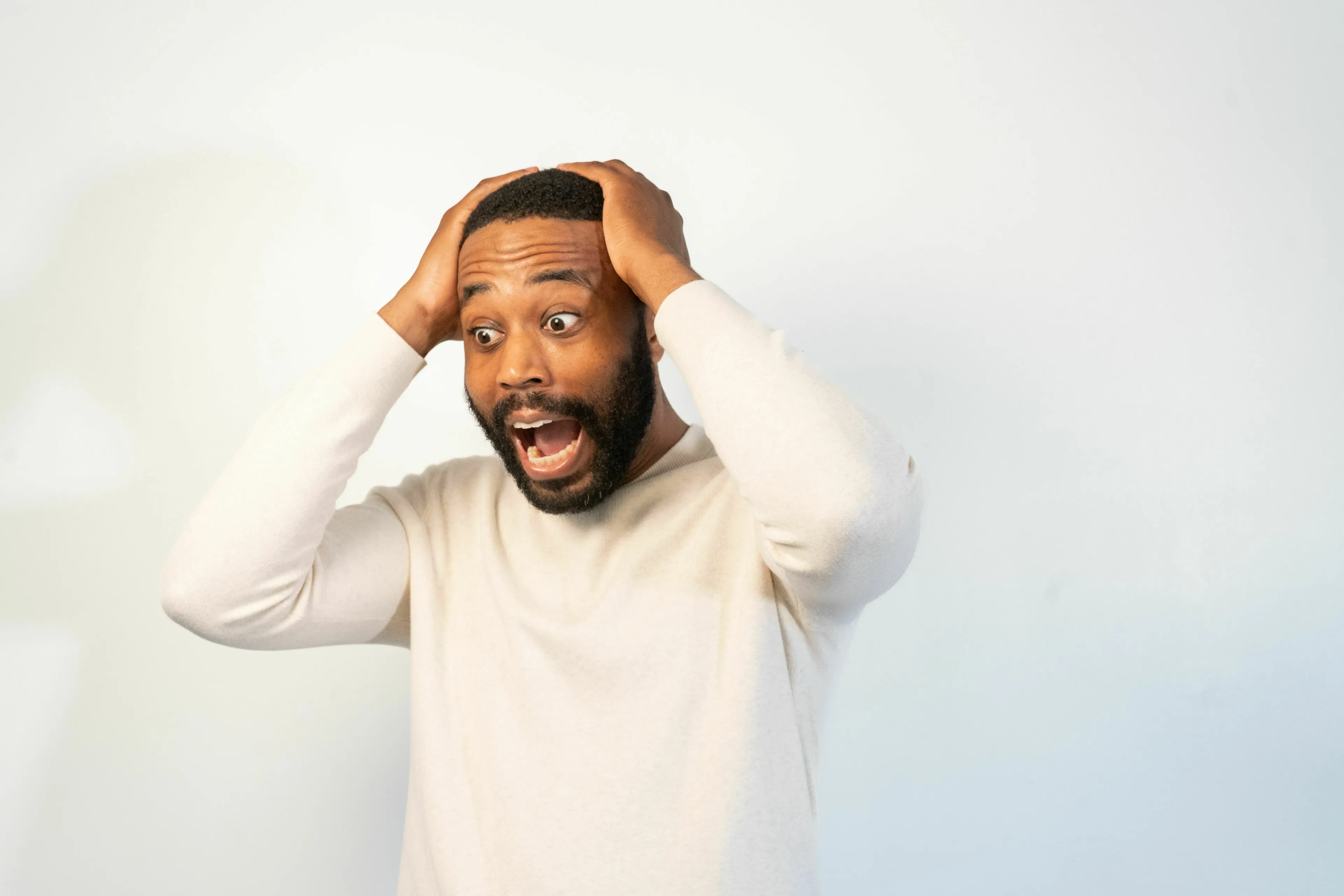 Man looking panicked, hands on head, reacting to a big deadline moving up, showing stress response.