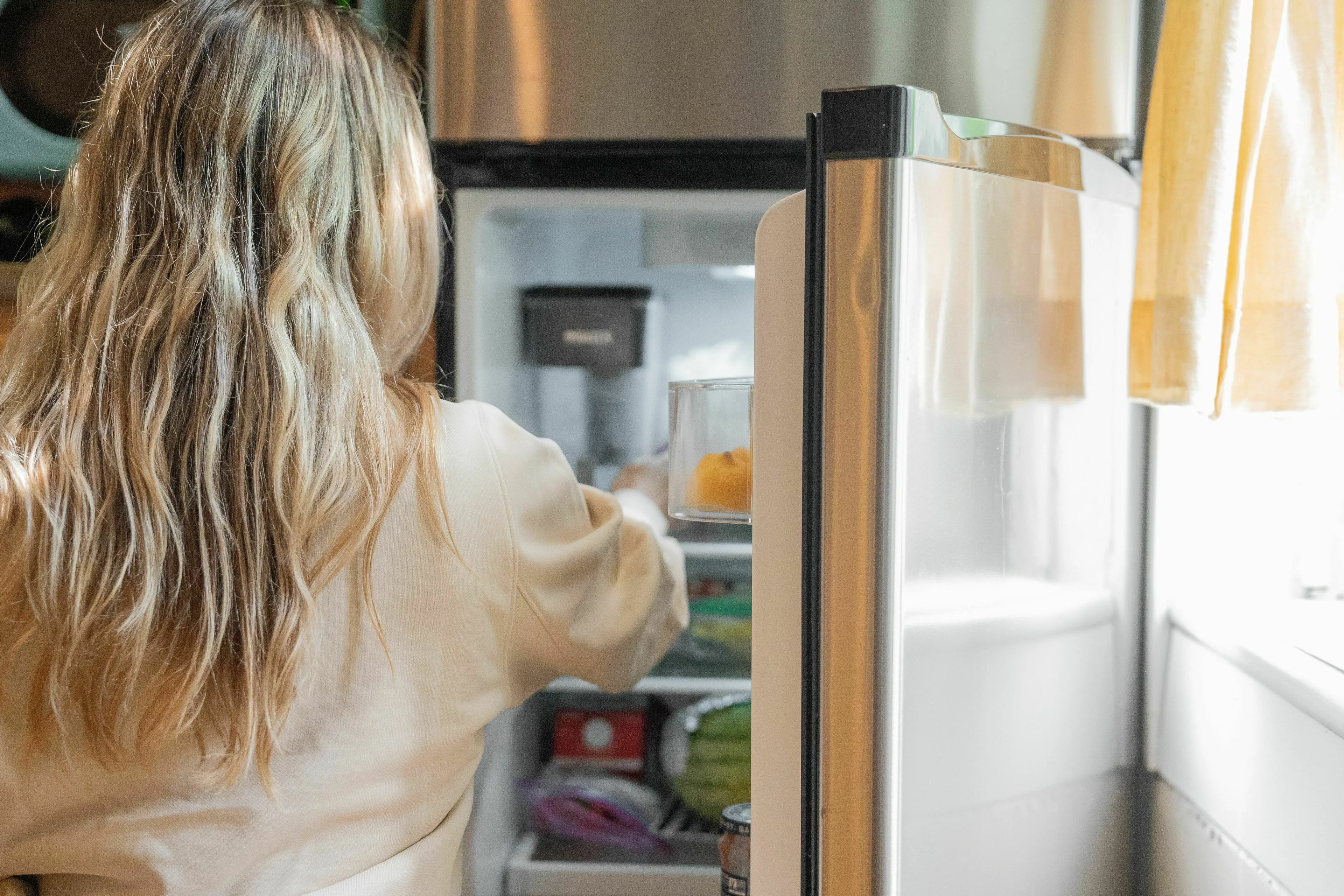 Woman opening refrigerator to pick a comfort food for a rough day, demonstrating stress response.