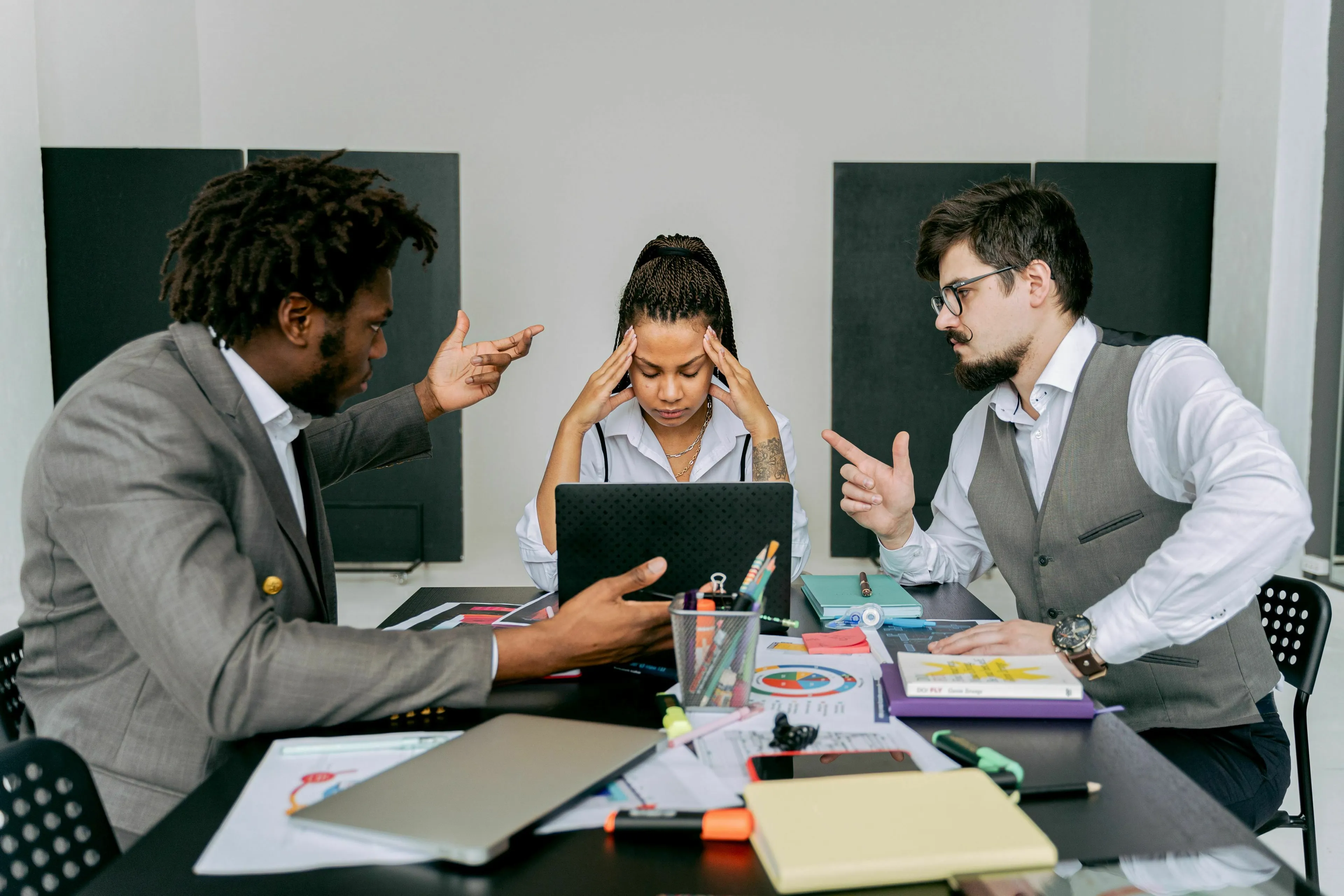 Discover your stress response type: a woman in a meeting looks stressed while two men argue about conflict.
