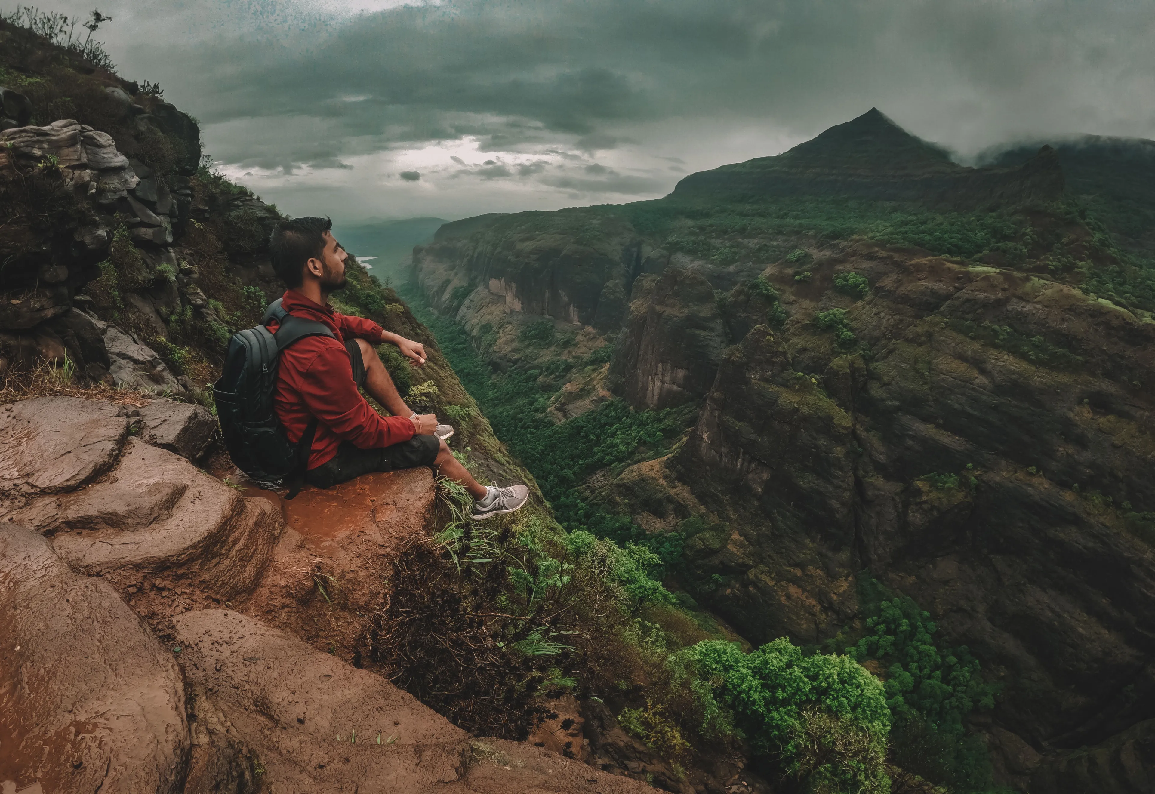 A man sitting on a cliff overlooking a valley, symbolizing an adventurous vacation spot.