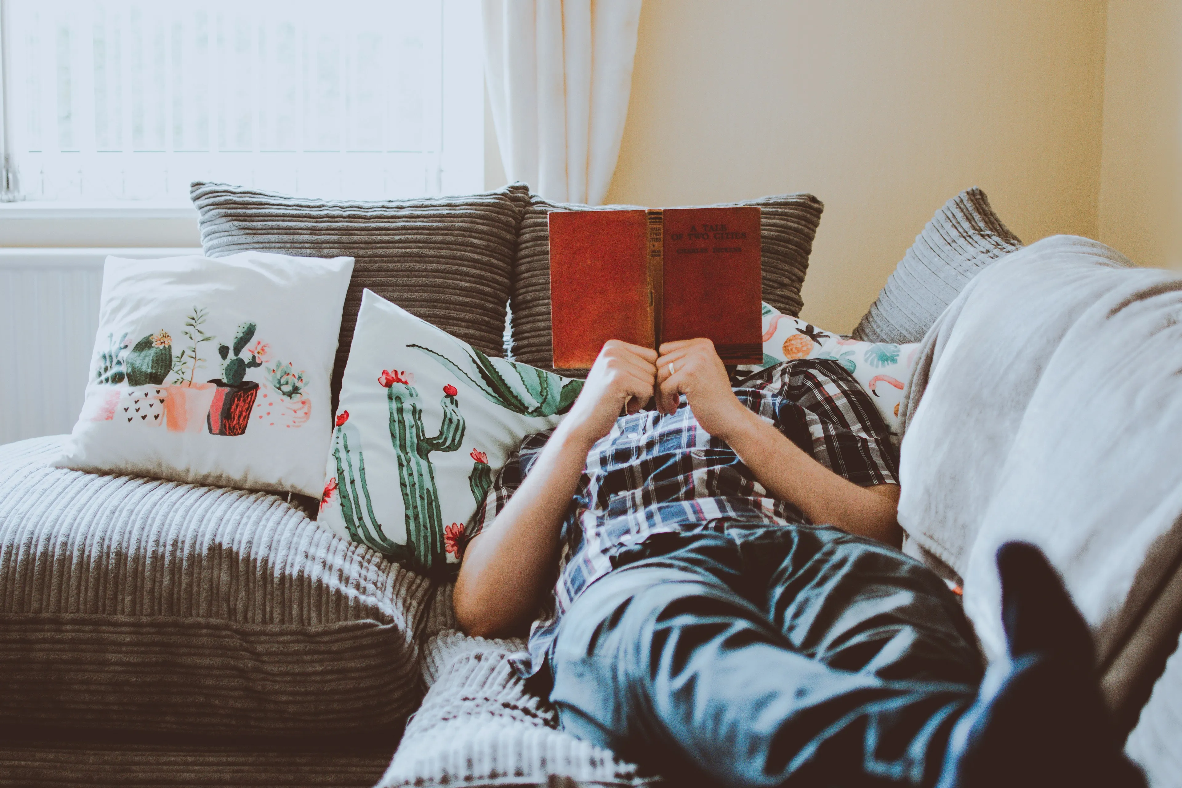 A person relaxing on a couch, reading a book, depicting home as a preferred vacation spot.
