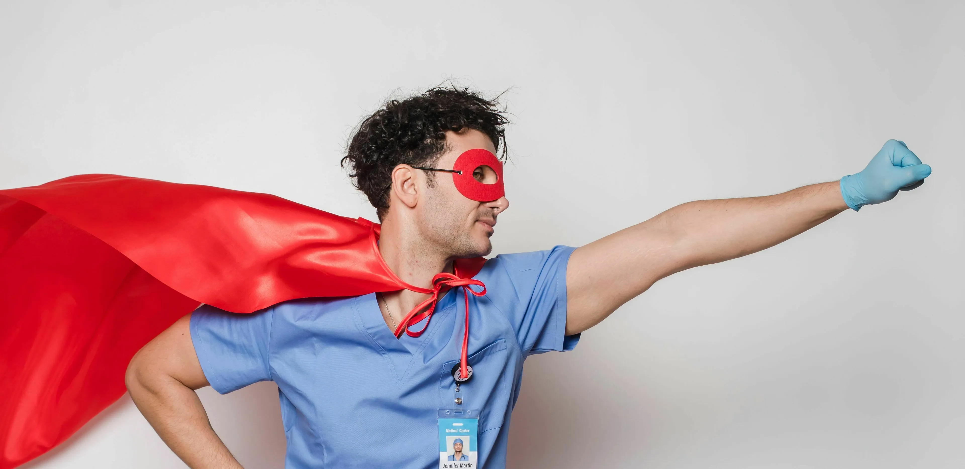 Man in scrubs, red cape and mask, portraying a superpower for a chaotic week, indicating stress response.