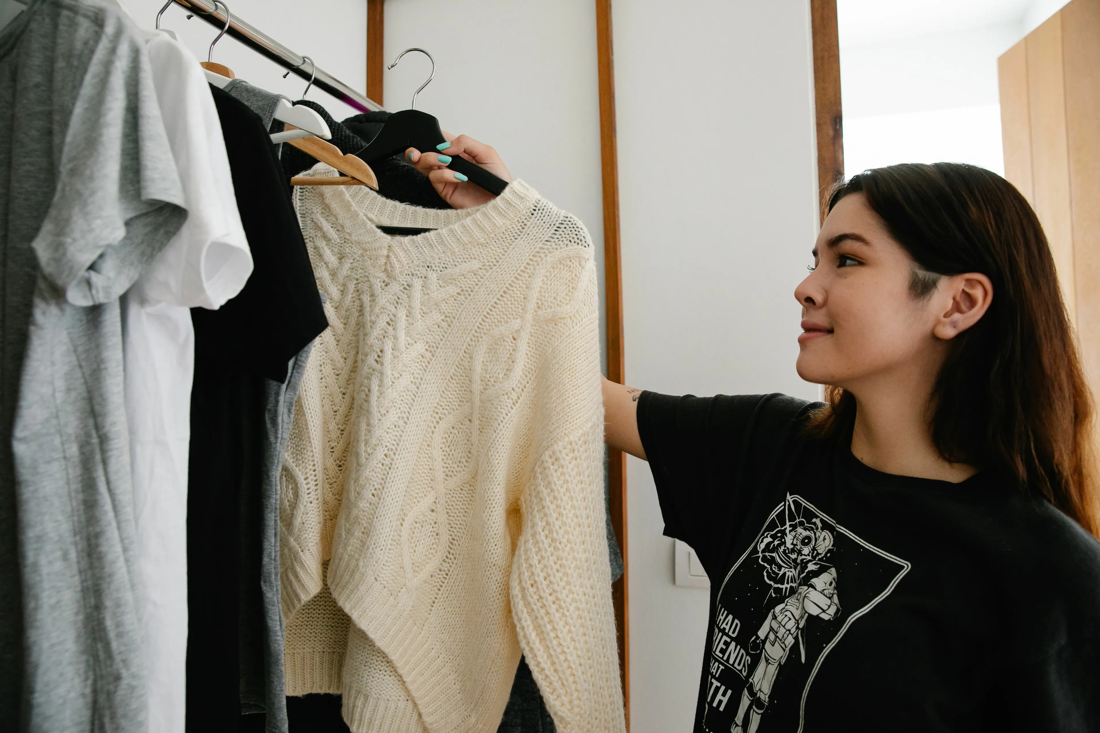 A person happily organizing their closet, holding up a cream-colored sweater on a hanger.