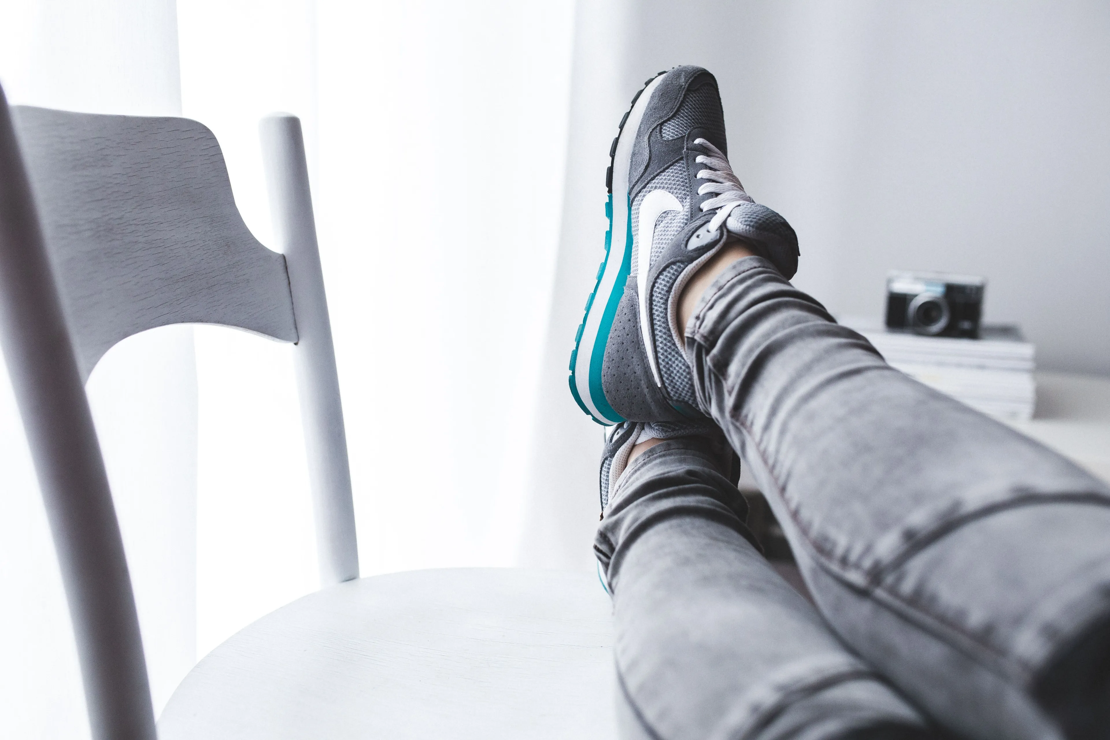 A person in grey jeans and sneakers, legs crossed on a white chair, enjoying a relaxing weekend activity.