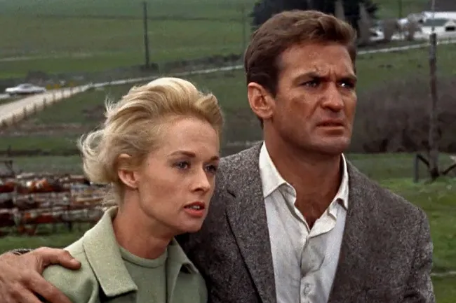 A dramatic still from the Hitchcock film The Birds, showing the main characters looking concerned.