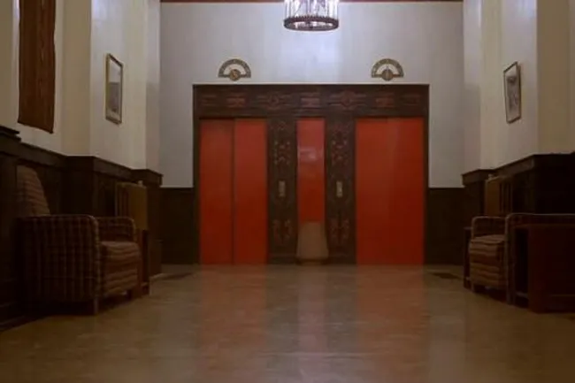 The iconic red elevator doors in The Shining, set in a deserted hotel hallway with chairs.