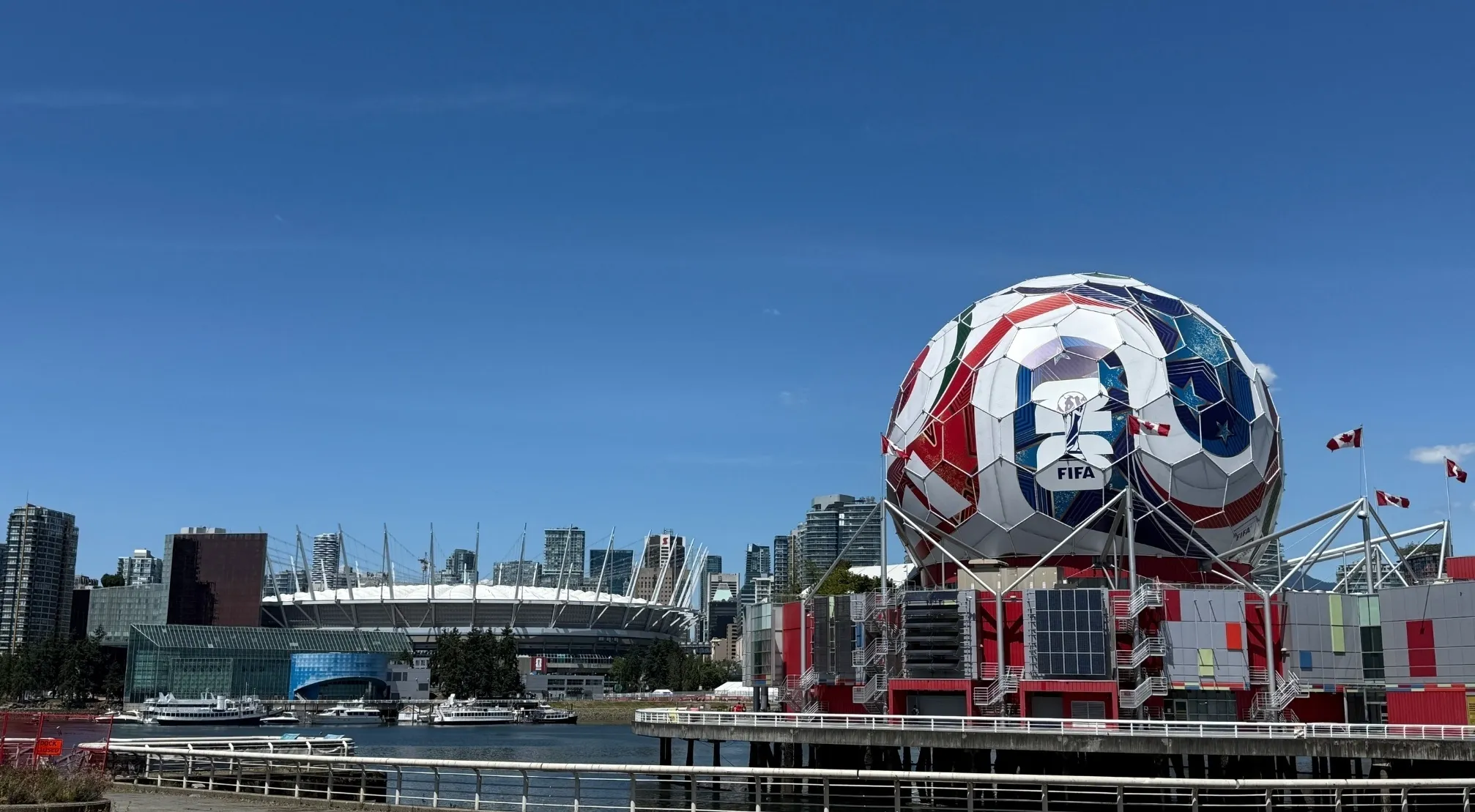 Giant FIFA World Cup soccer ball display on waterfront with stadium and city skyline in background.