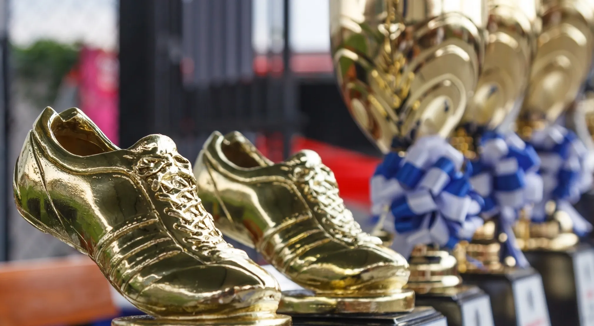 Golden boot trophies shaped like soccer shoes, with blurry championship cups in the background. A FIFA World Cup quiz visual.