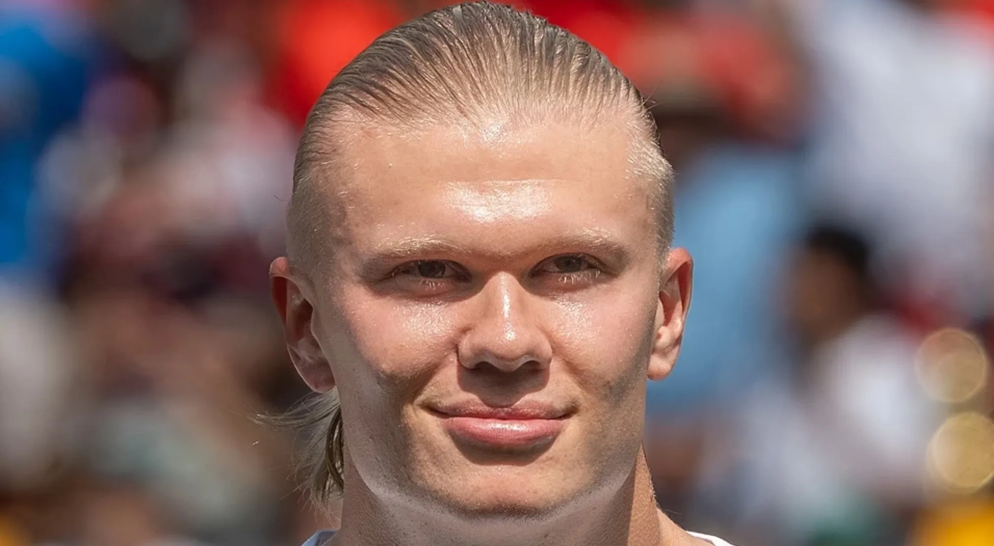 Close-up of a famous FIFA World Cup player, fair-skinned with slicked-back blonde hair and a faint smile.
