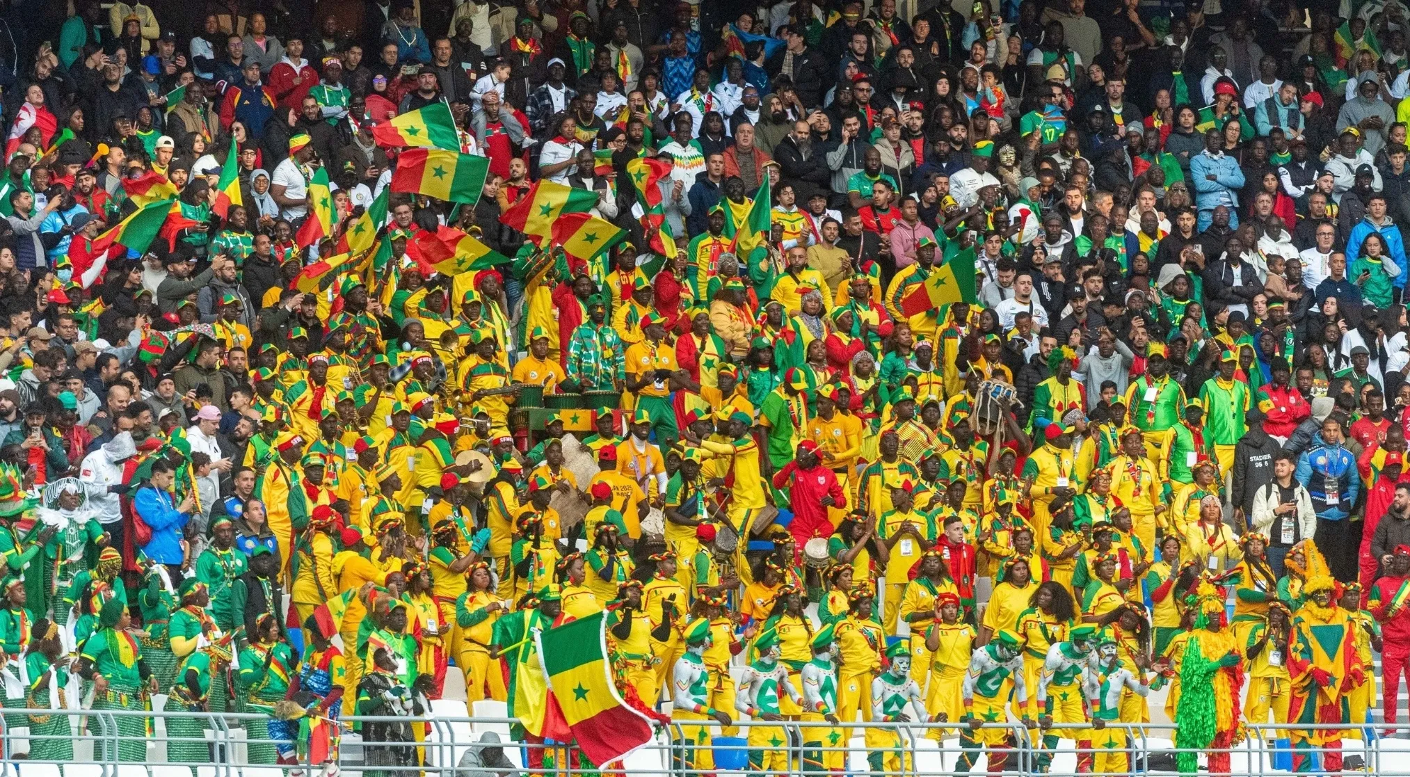A vibrant crowd of FIFA World Cup fans, mostly in yellow and green, waving Senegalese flags.