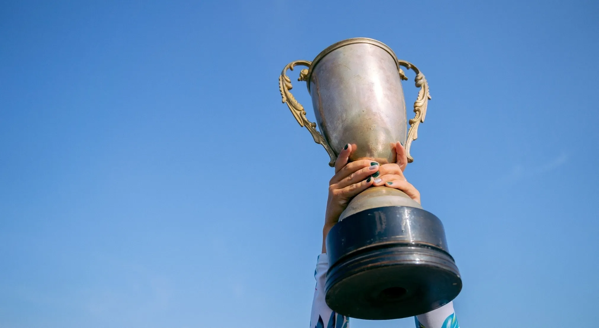 Hands holding a trophy high against a clear blue sky. Reflects FIFA World Cup wins.