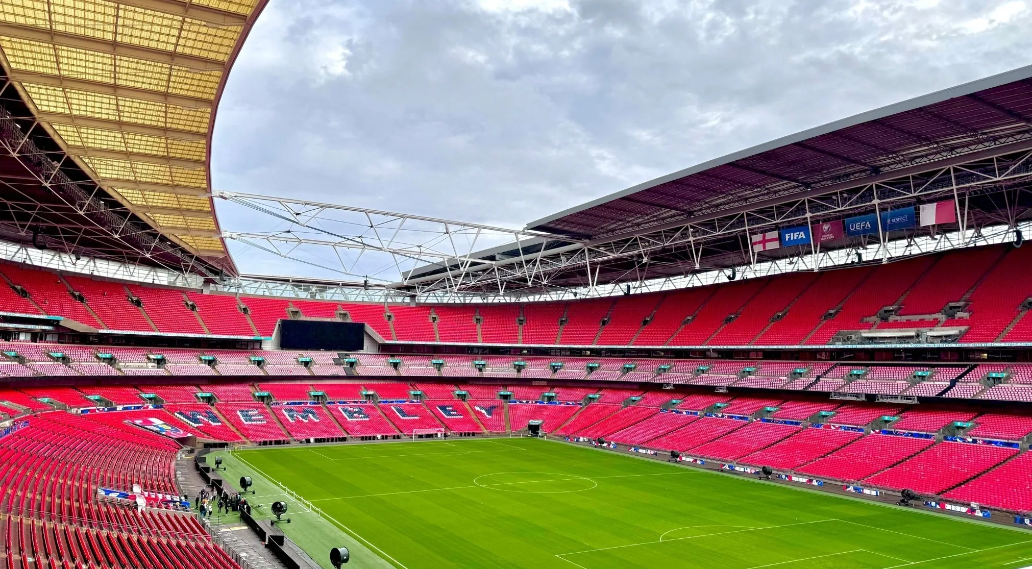 An empty, vibrant green football field at Wembley Stadium with rows of red seats, home to many FIFA World Cup Final contenders.