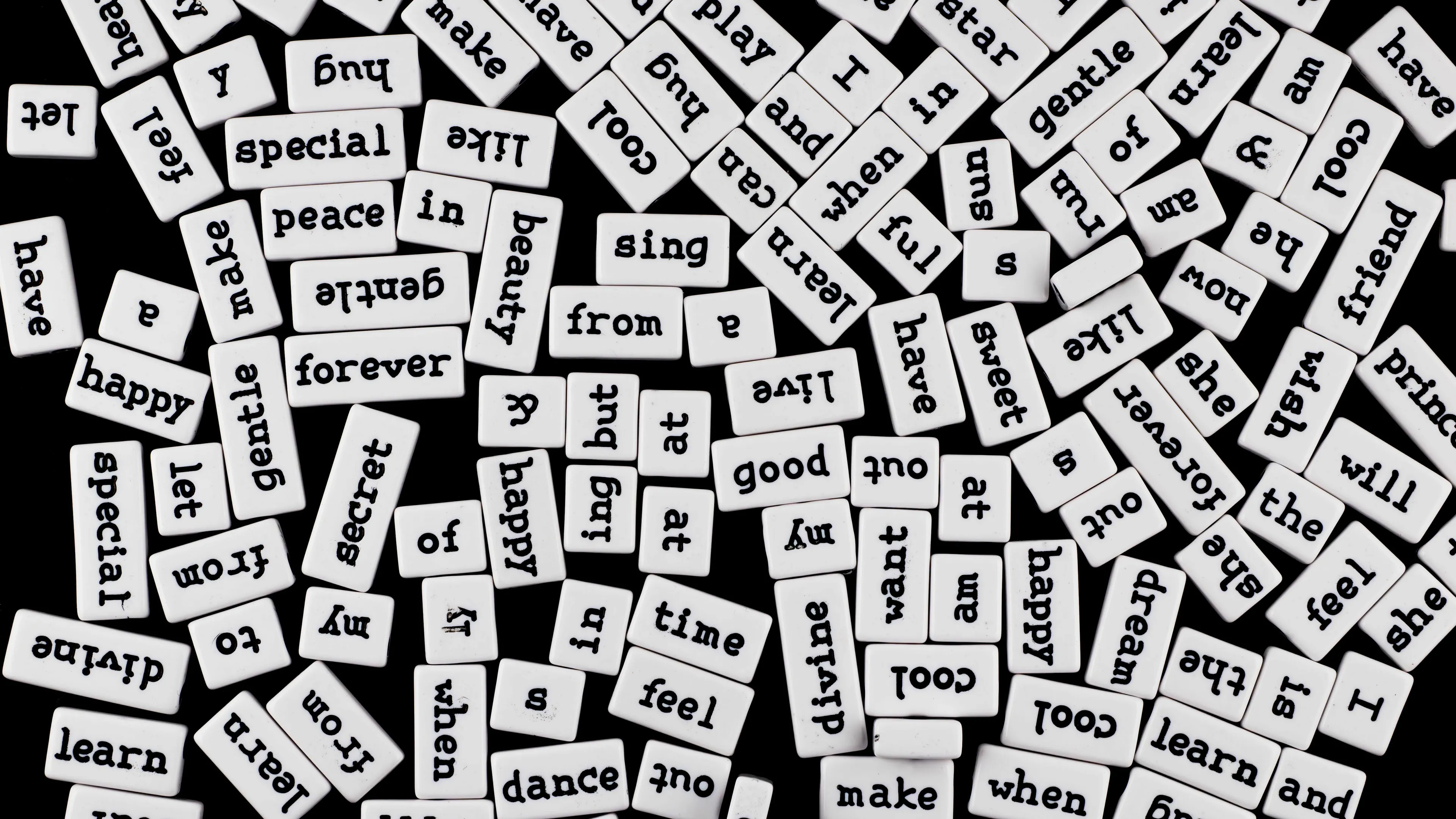 A pile of white word tiles with various English words, scattered on a black surface, representing a word with the same meaning.