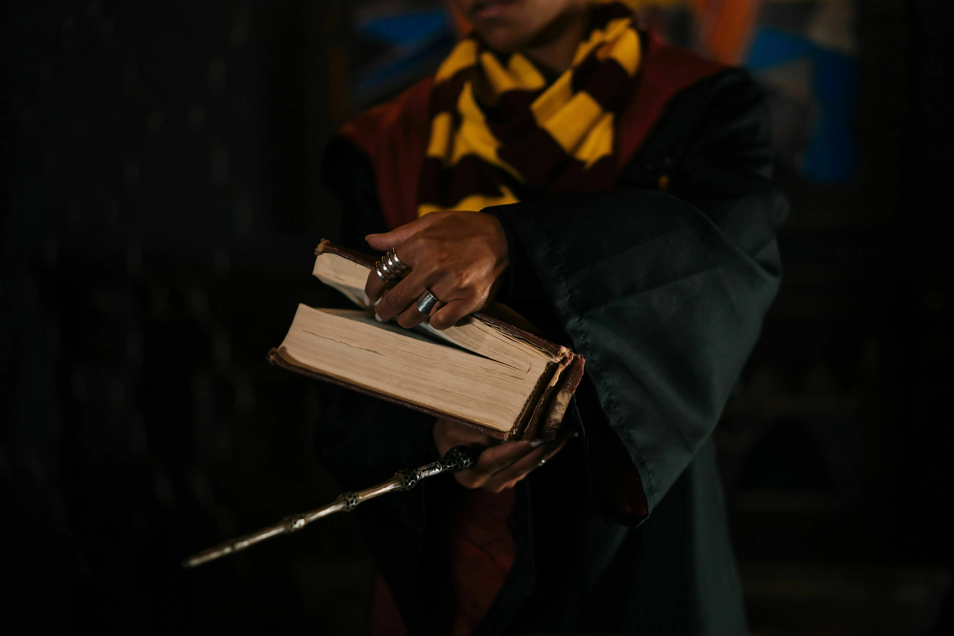 Person in wizard robes holding books and a wand, referencing the young wizard created by J.K. Rowling for a Pub Trivia Quiz.