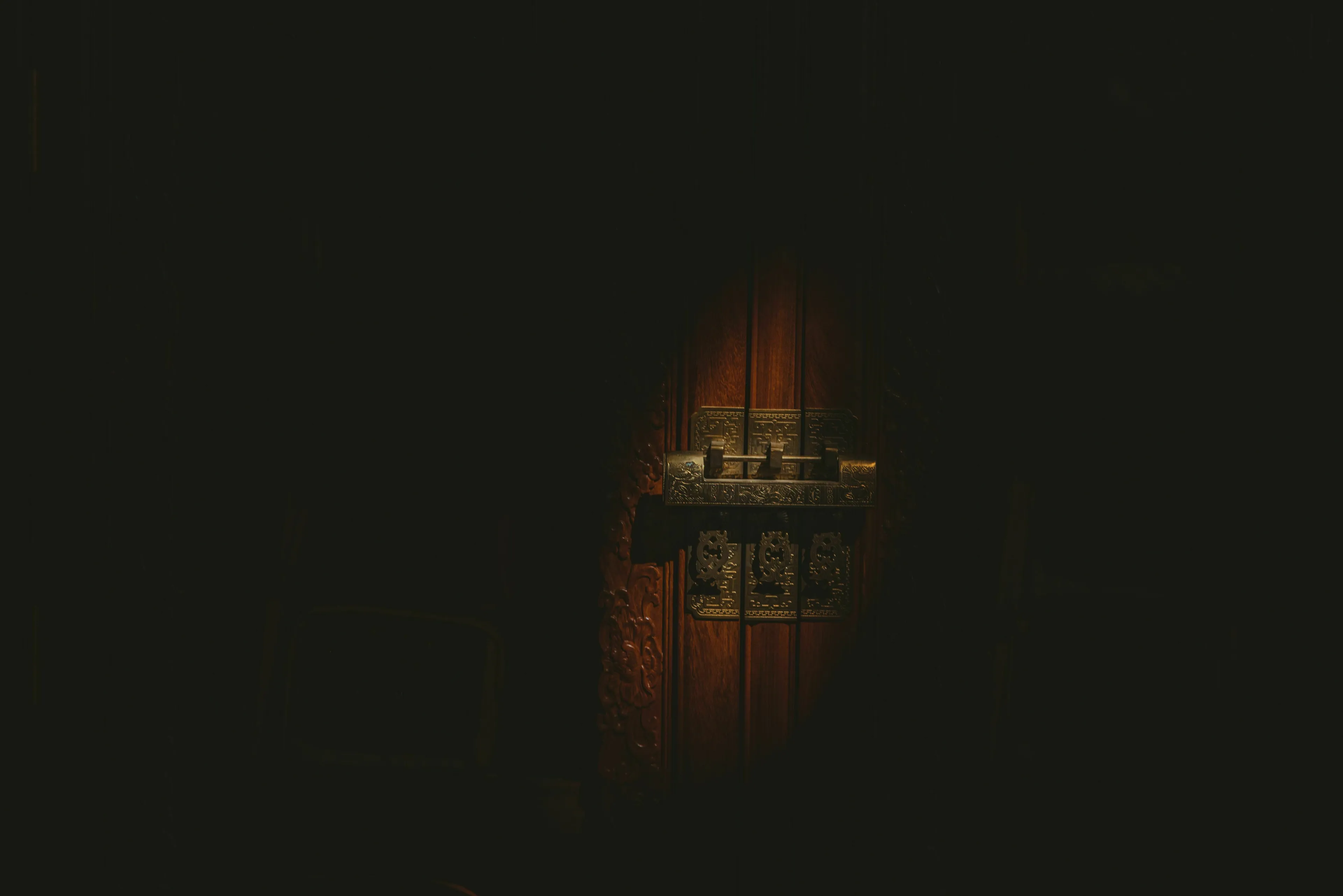 A dark room with a spotlight on an old, ornate wooden door and its metal latch, representing a relationship with rules.