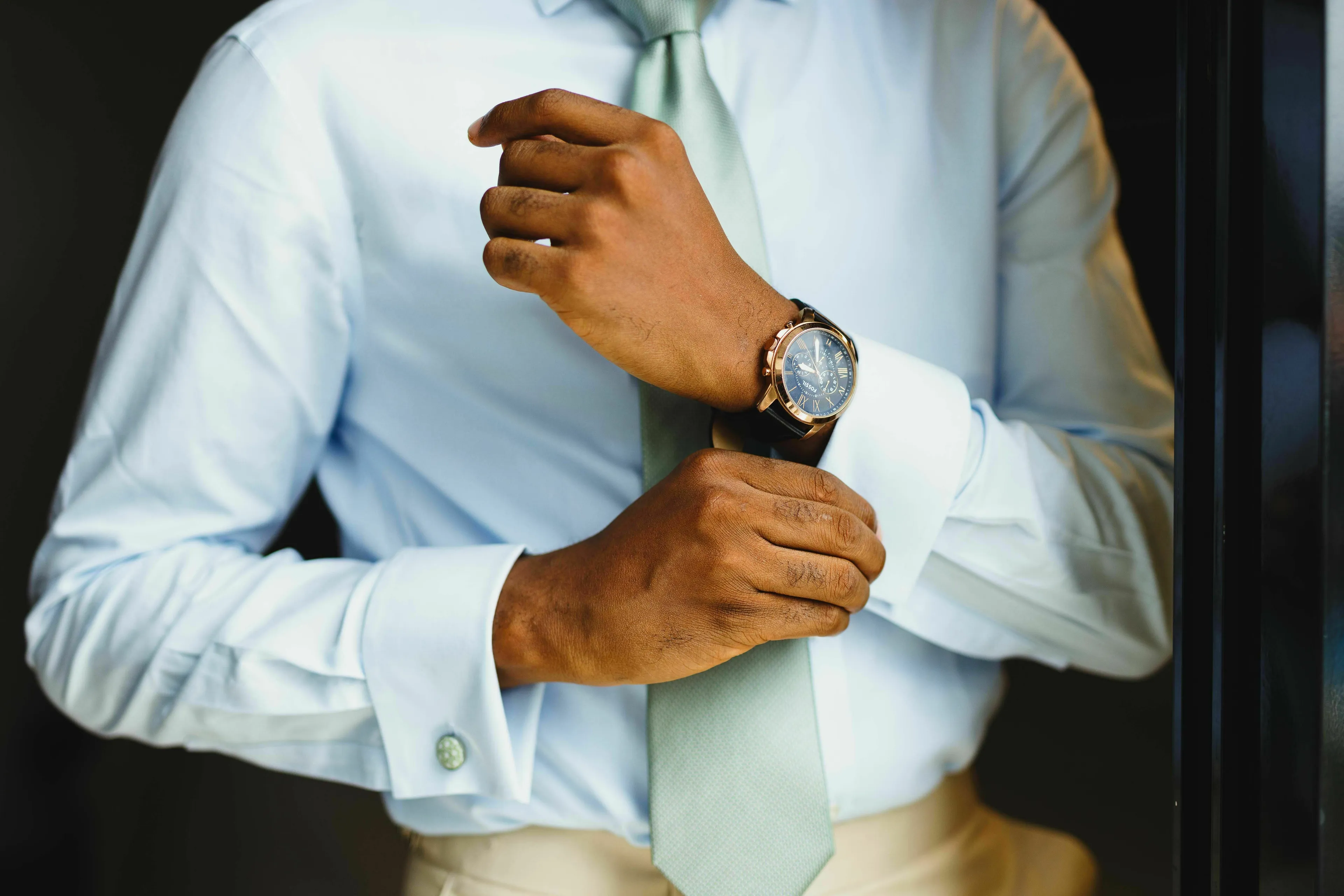 A man adjusting his cufflink, representing a new office dress code memo and personal reaction to rules.