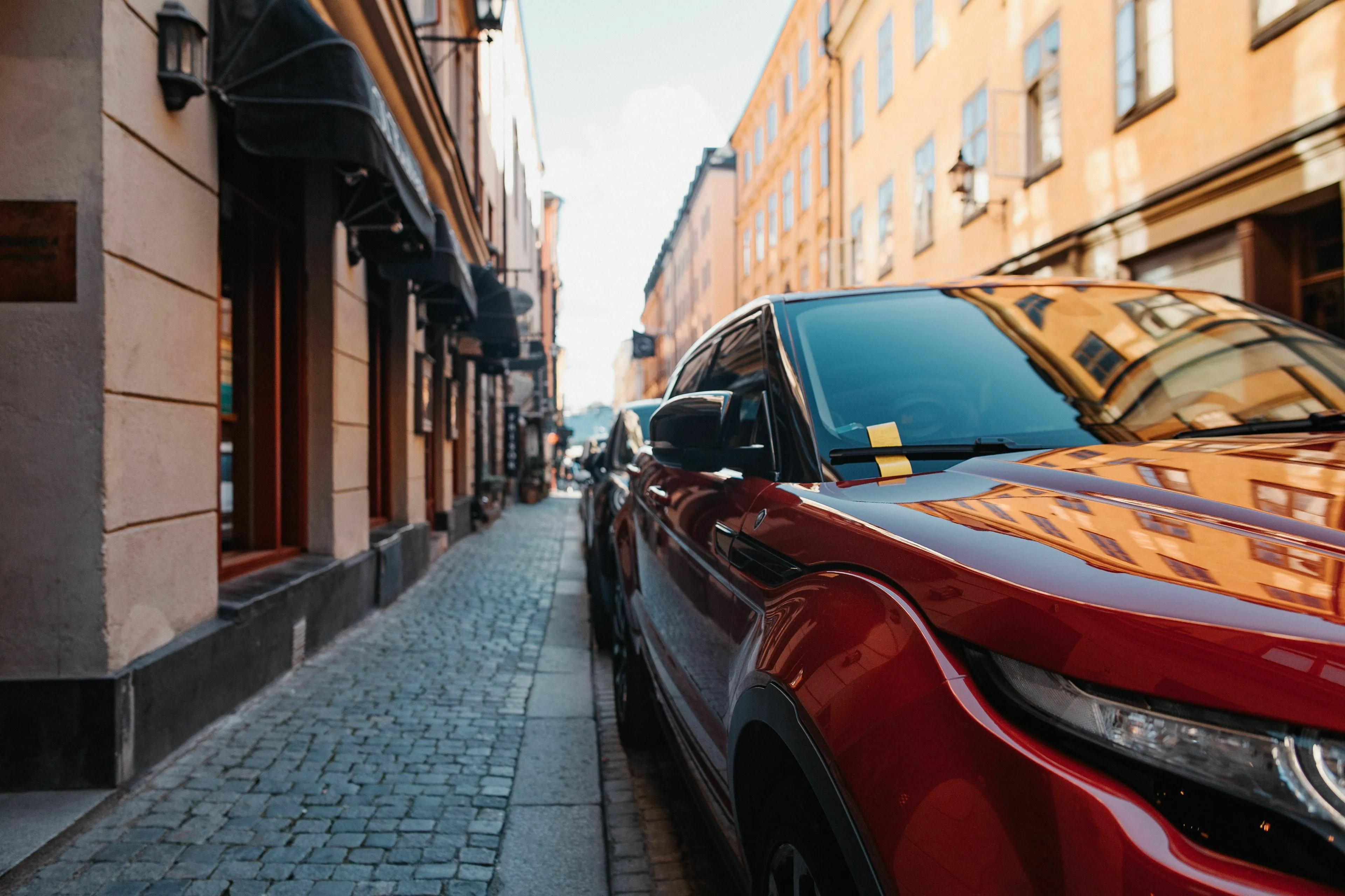 A red car with a parking ticket on its windshield, parked on a cobblestone street, highlighting relationship with rules.