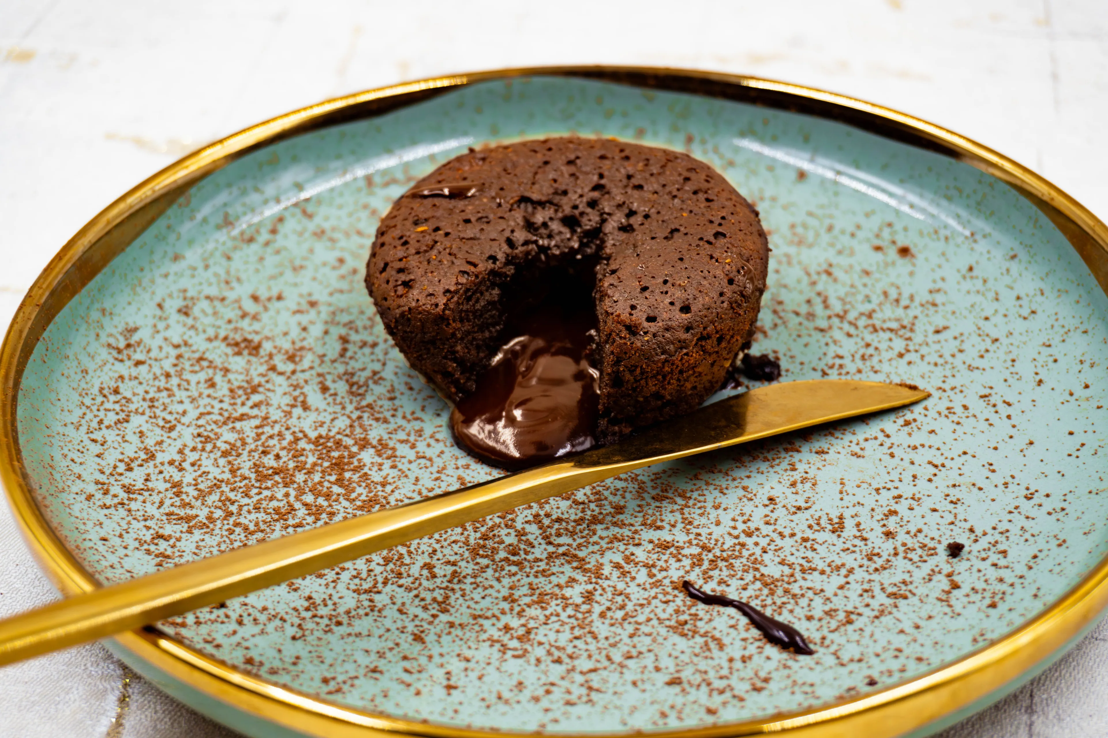 Delicious chocolate lava cake on a teal plate with a golden knife, dusted with cocoa powder.