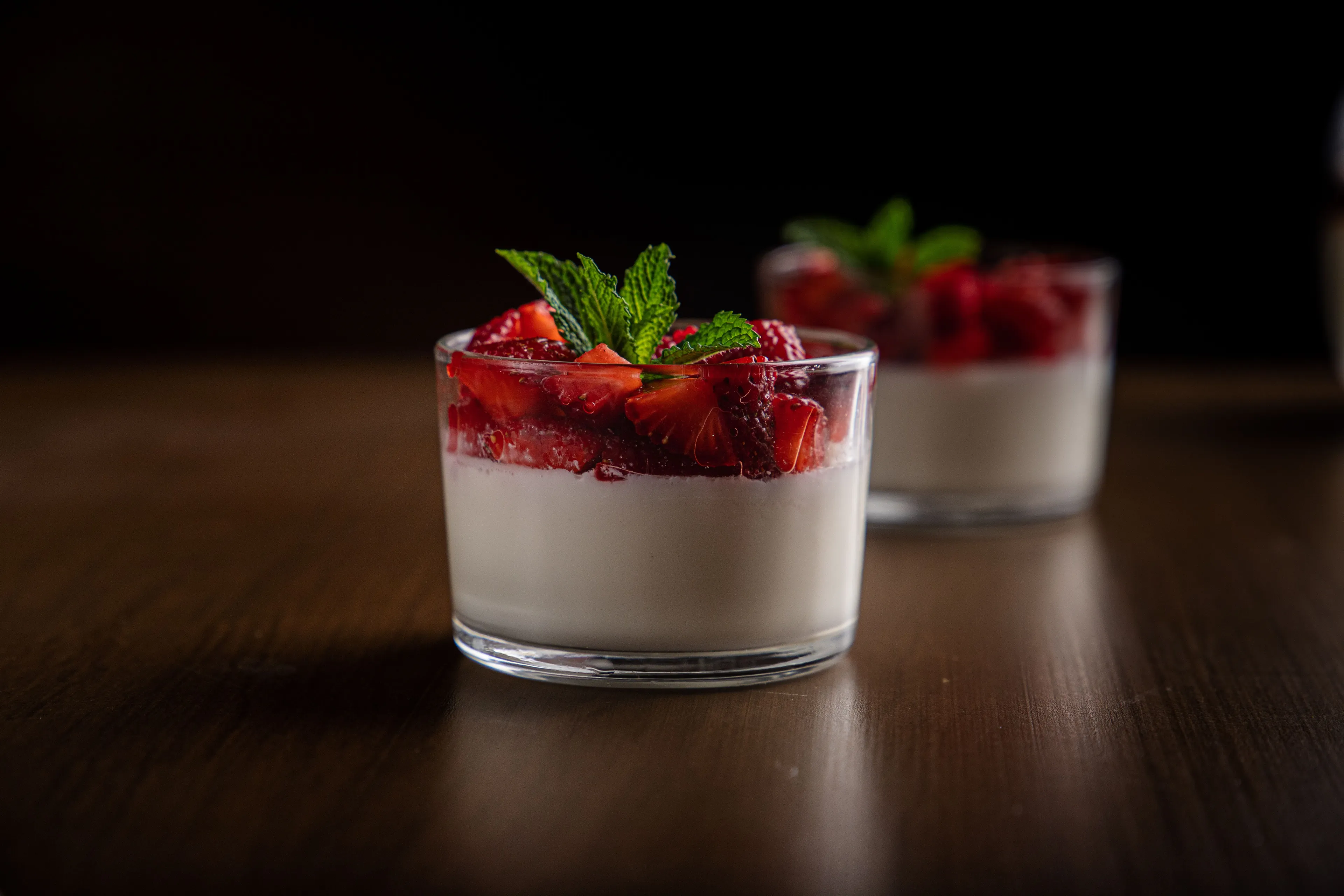 Two glasses of creamy panna cotta topped with fresh strawberries and mint leaves.