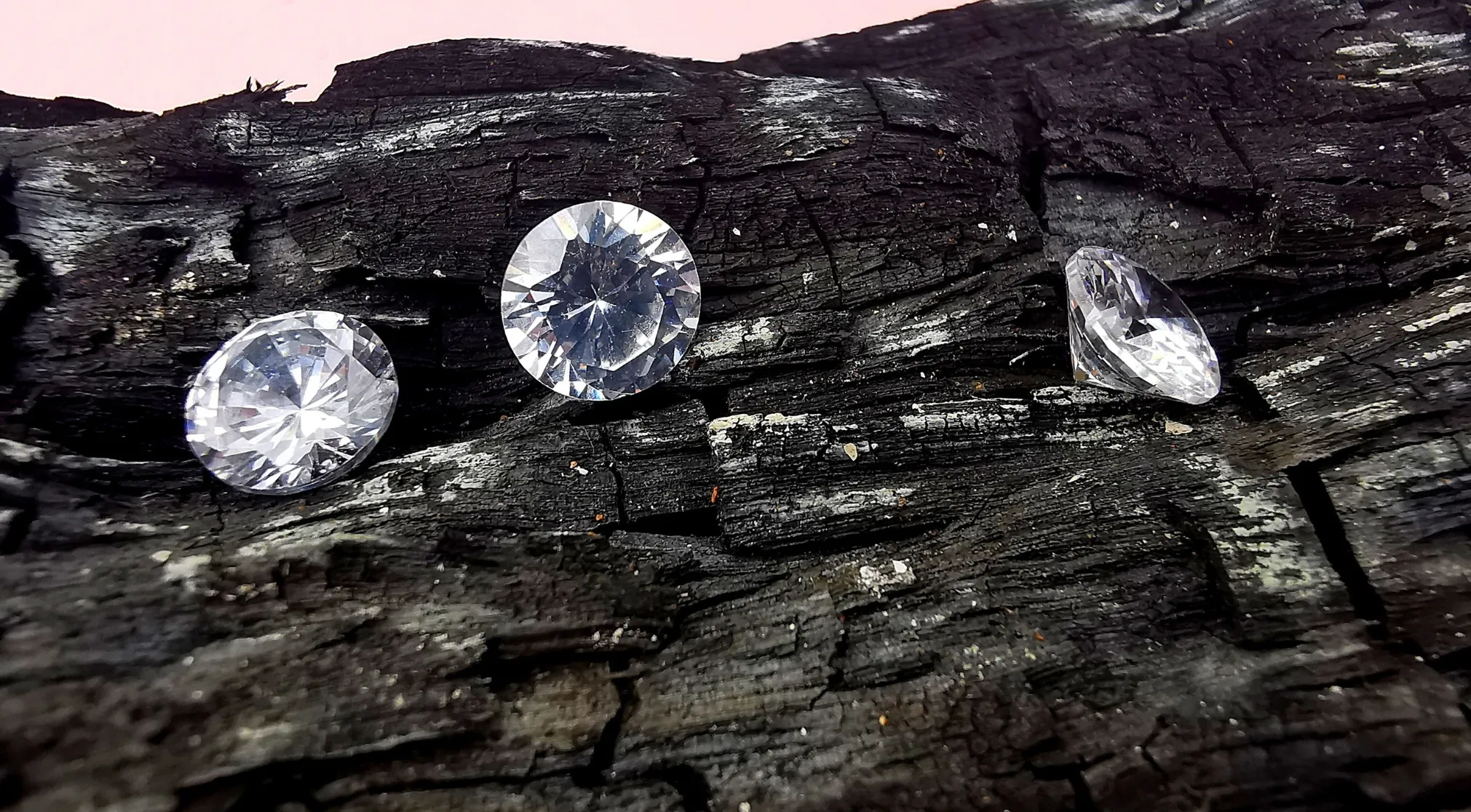 Three glittering diamonds rest on a charred, dark wood surface, illustrating the WWI Recruit Test question: Are diamonds mined in mid-ocean?