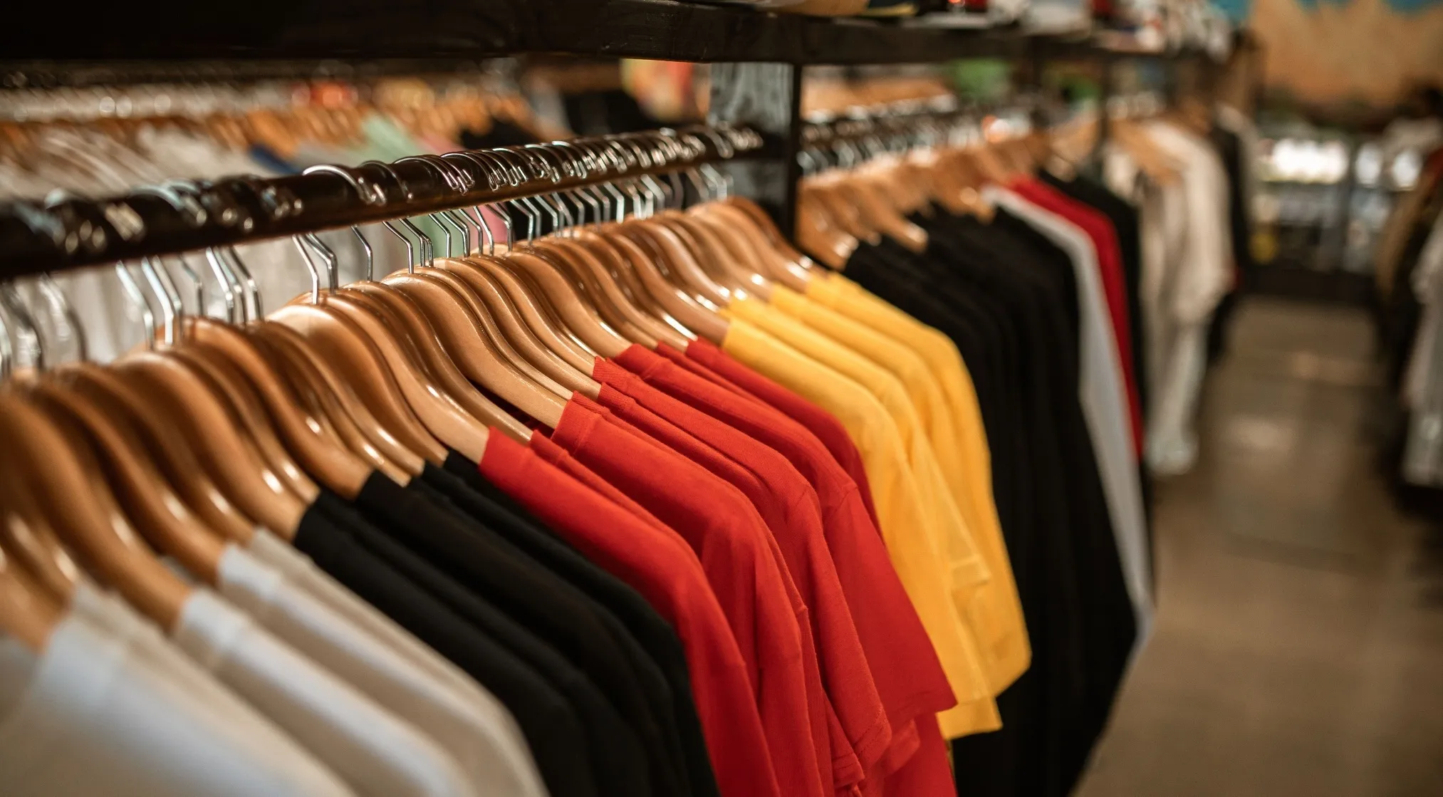 Rows of colorful t-shirts hang on wooden hangers in a store. WWI recruit test question: Should fathers provide clothing for children?