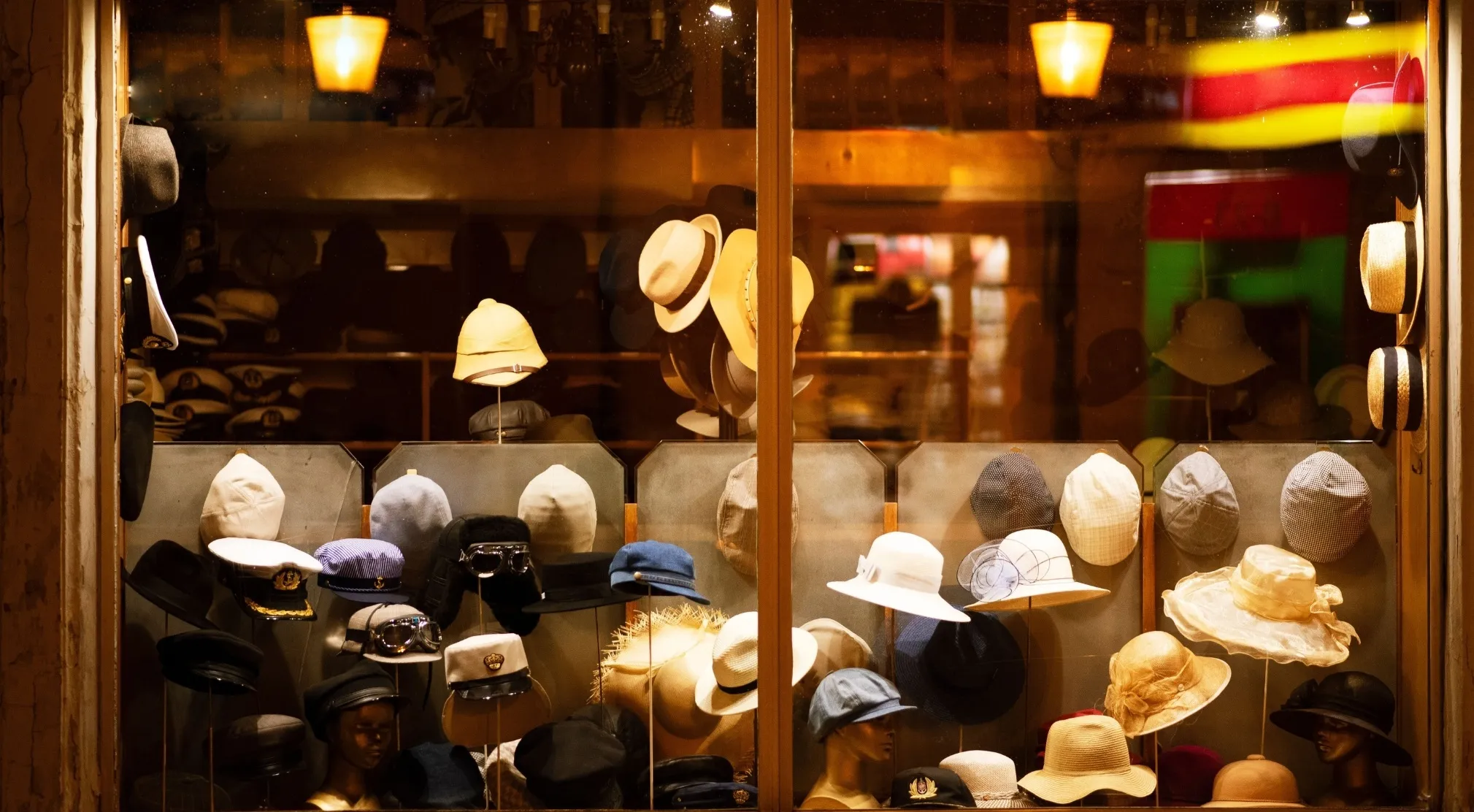 A window display of a hat shop, with various styles of hats on mannequins and shelves, including WWI recruit test era styles.