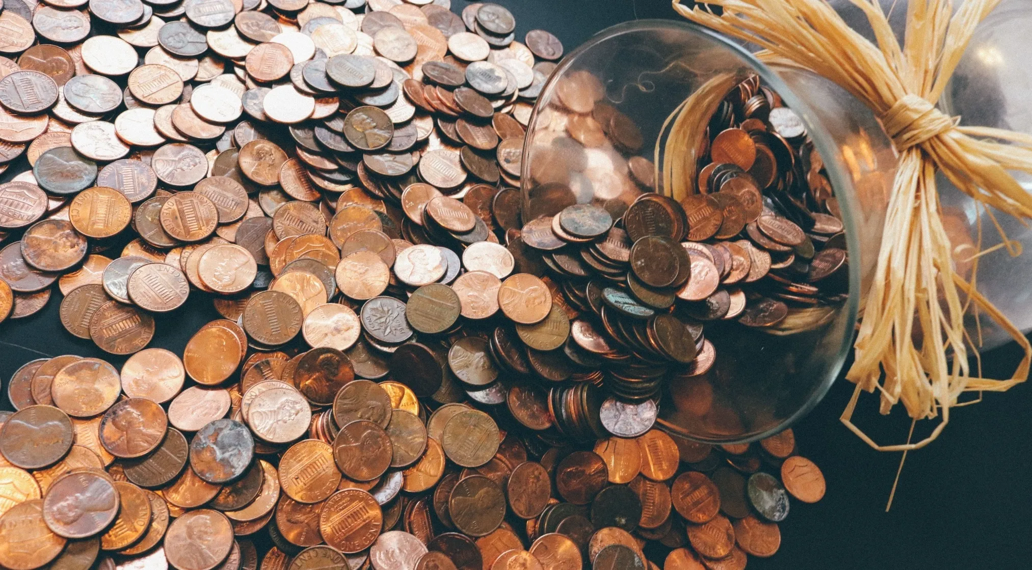 A pile of copper pennies spilling from a glass jar with straw, illustrating the concept of how many cents make a dollar.