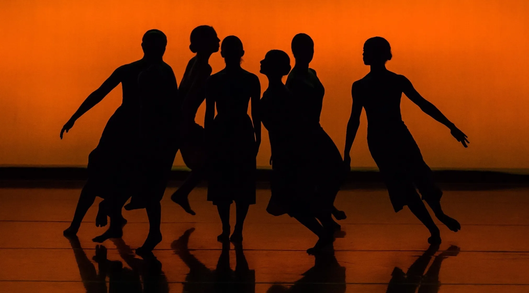 Silhouetted dancers against an orange backdrop, capturing movement and form, for a Jeopardy quiz on classic dance.