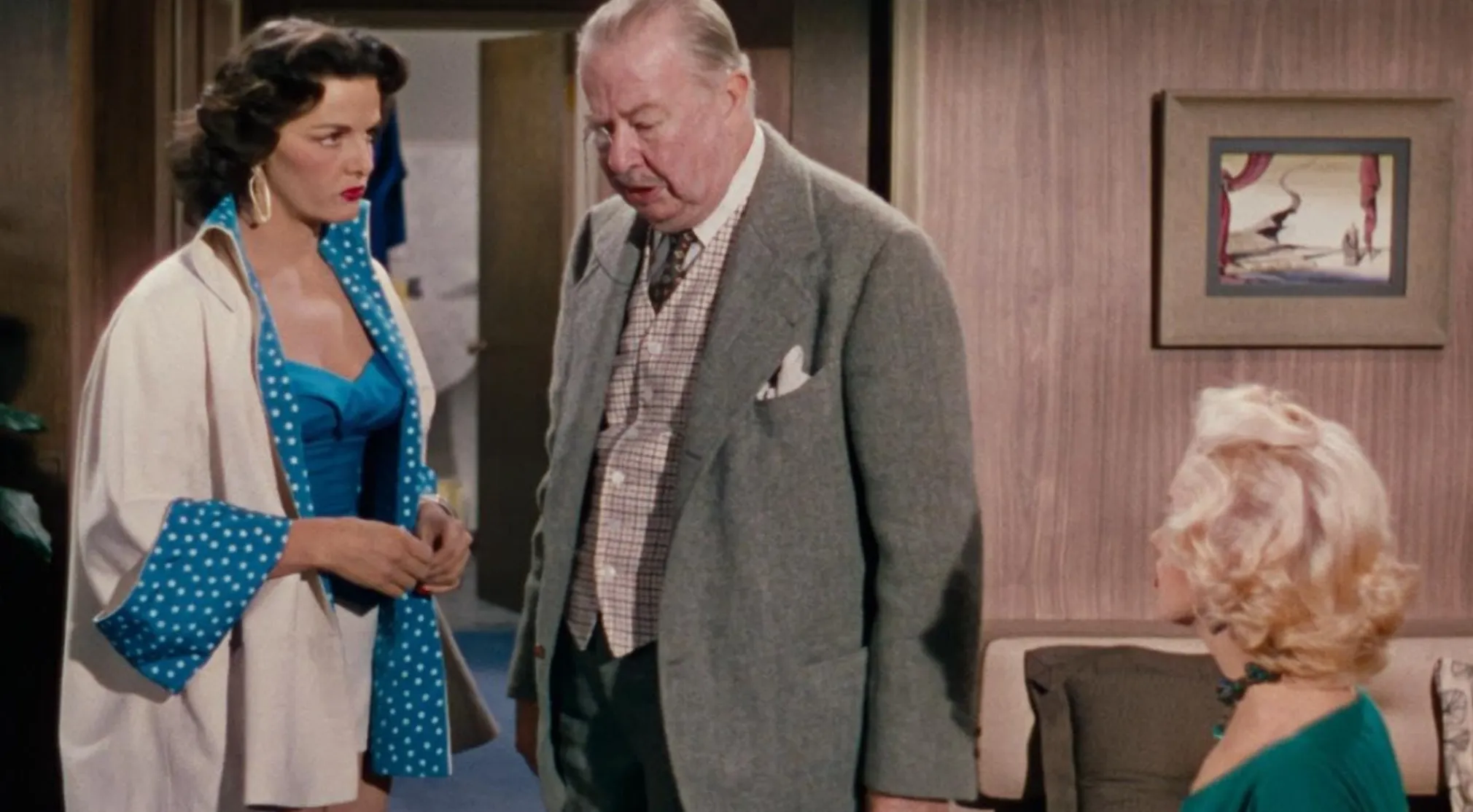 A Real Jeopardy Quiz Movies scene with a brunette woman in a blue top and robe, a man in a suit, and a blonde woman.