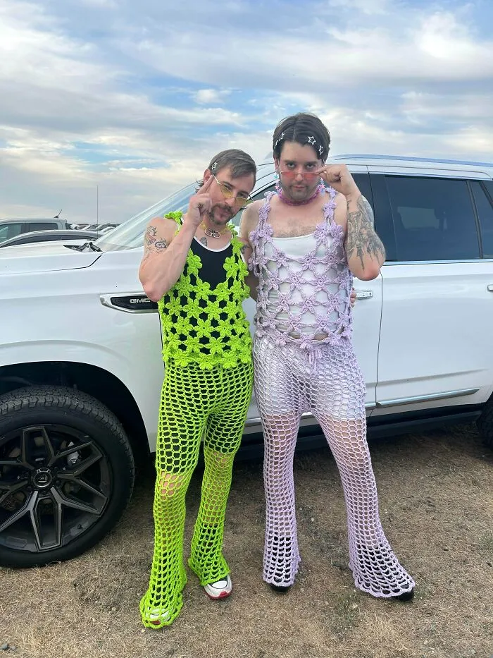 Two men wearing colorful crochet outfits posing by truck creative crochet project