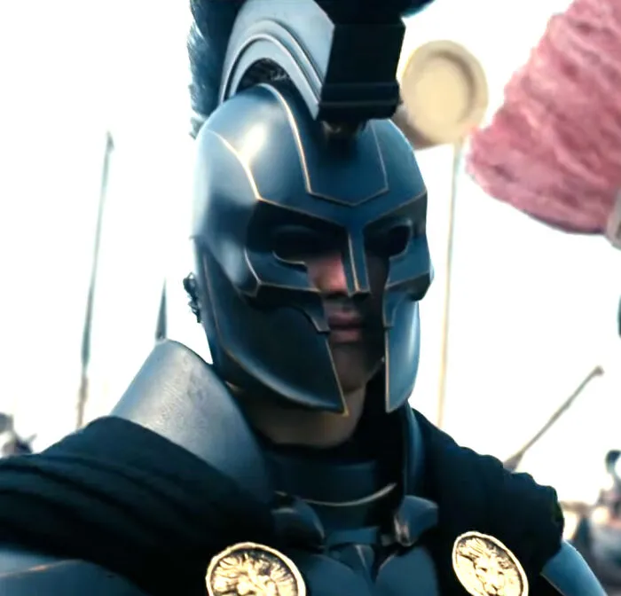 A close-up of a person in a dark, ornate Greek-style helmet and armor, suitable for mythology memes.
