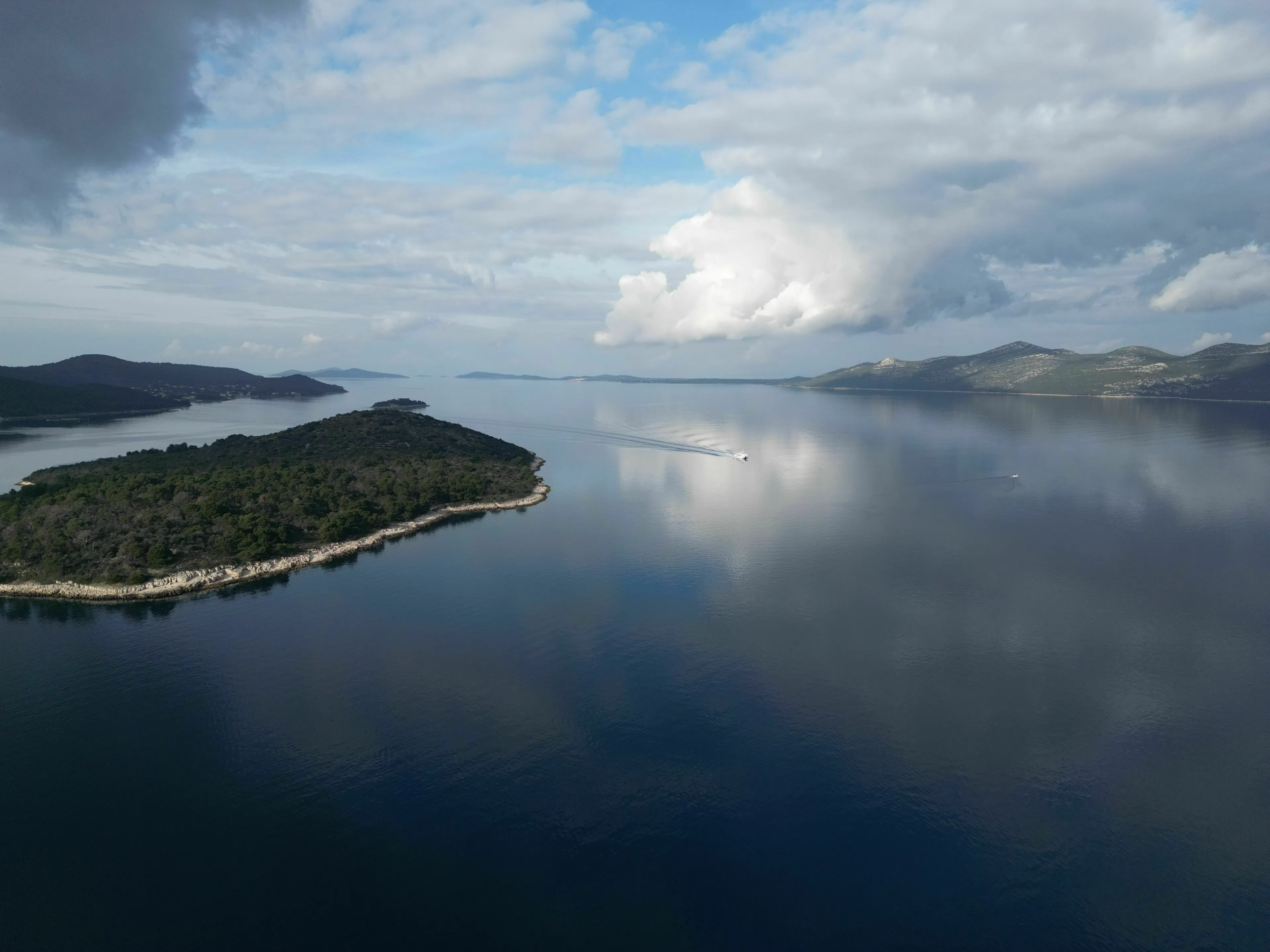 Aerial view of a boat on calm water near a wooded island, reflecting the sky, which extinct species