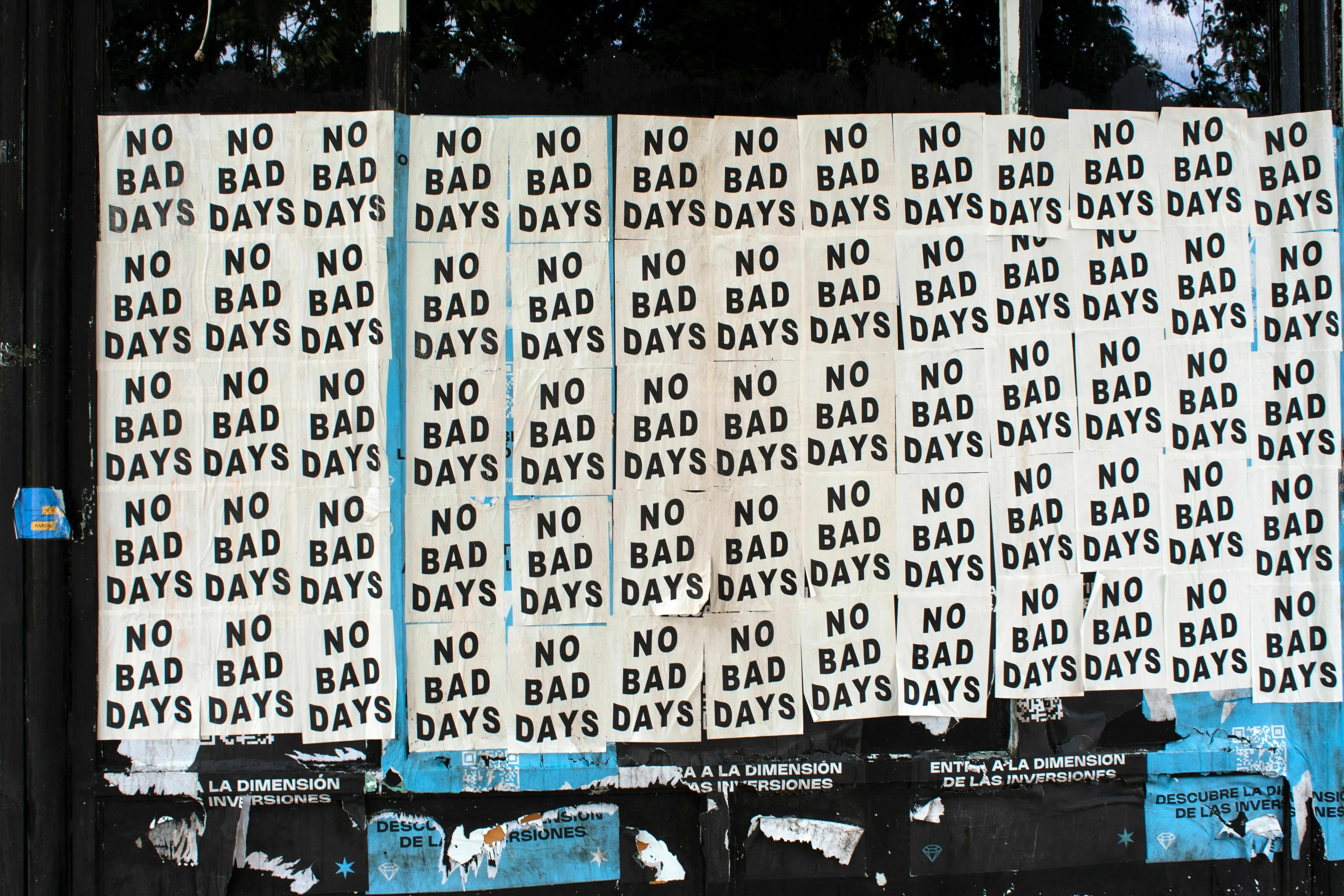 A wall covered with multiple posters repeating the phrase NO BAD DAYS, representing brutally hard times